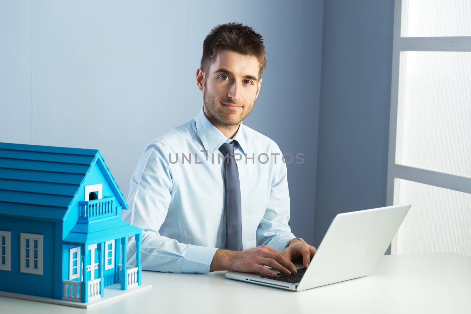 Man working with laptop at his desk and model house.