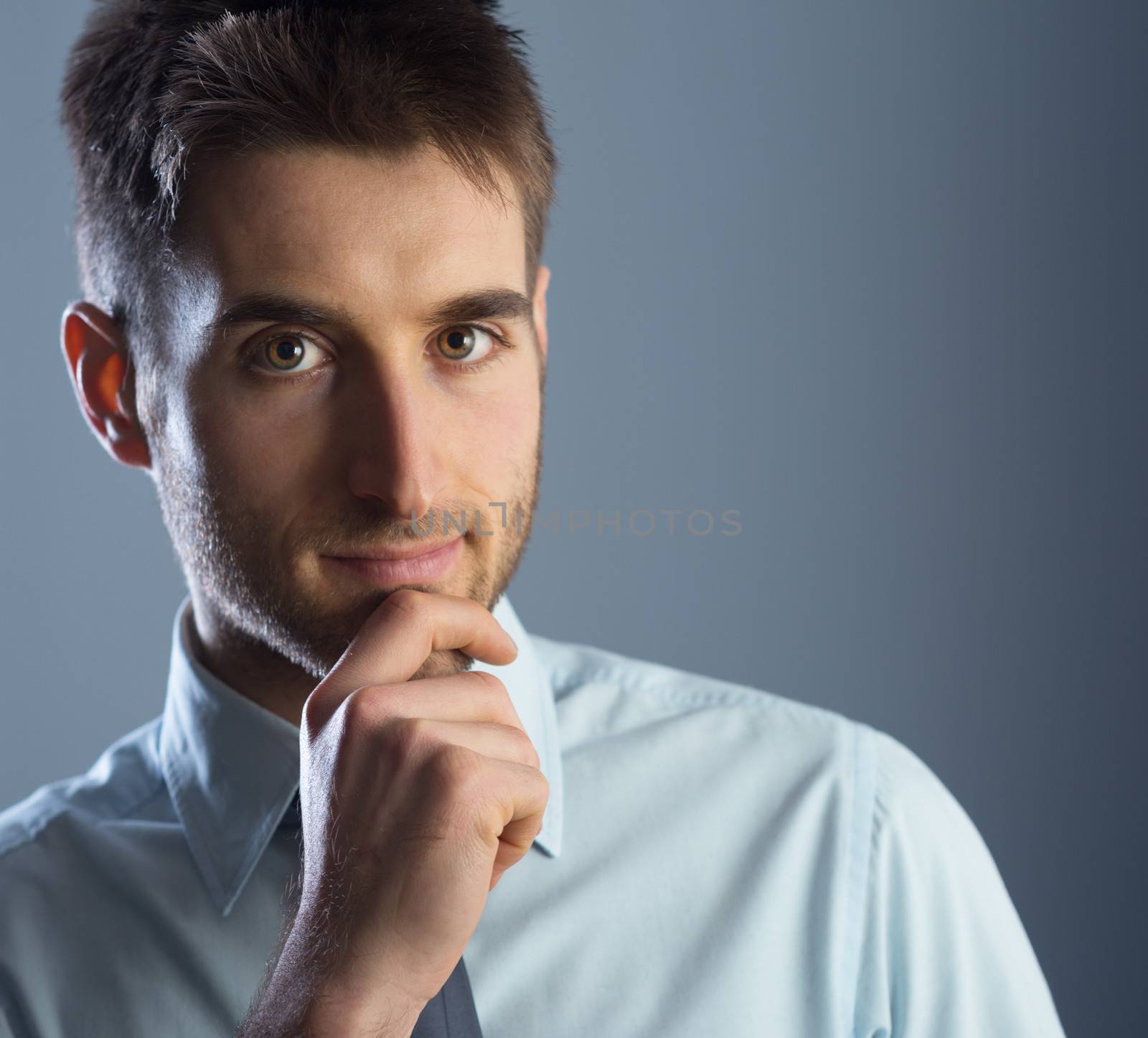 Young businessman with hand on chin, looking at camera.