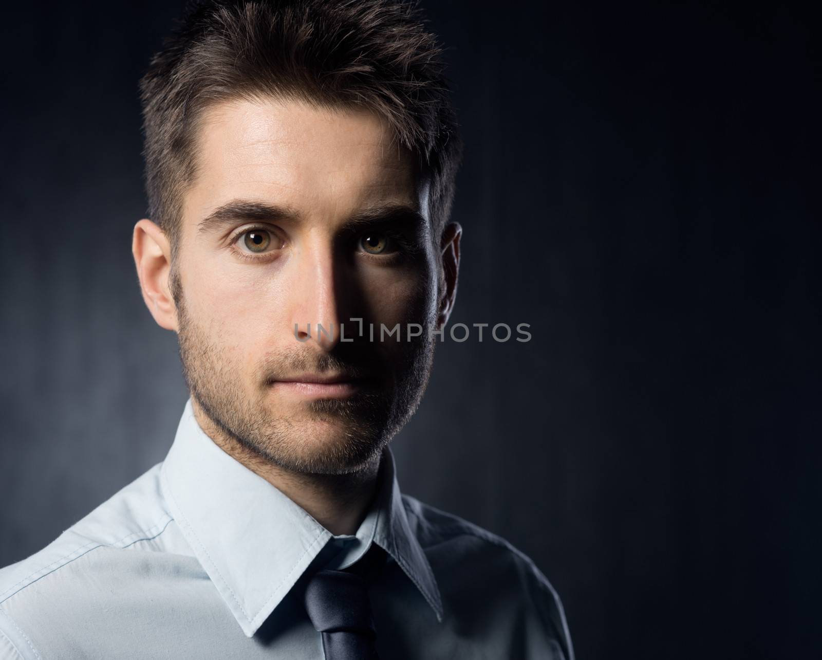 Confident businessman looking at camera on dark background.
