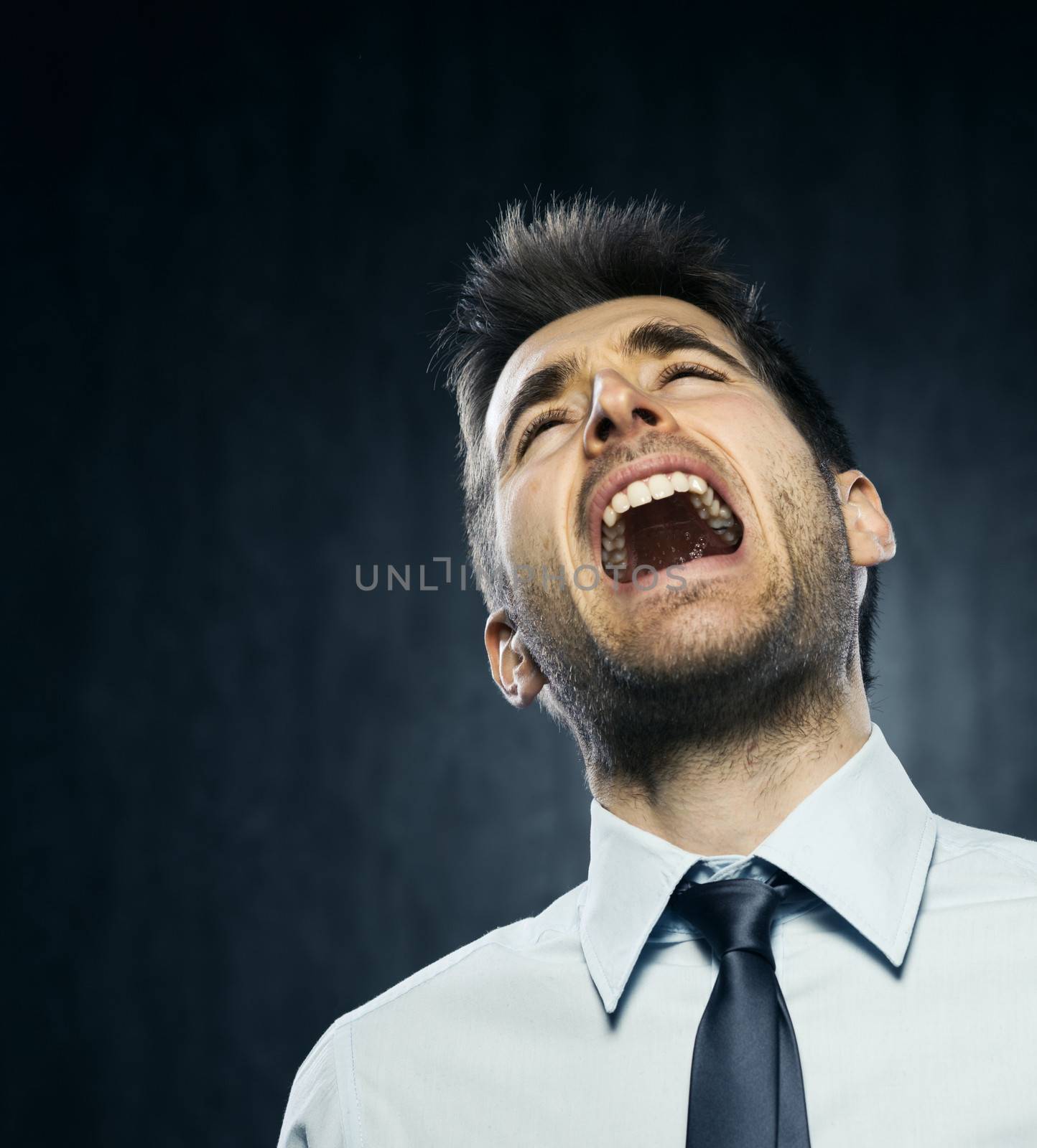 Furious young businessman on dark gray background.