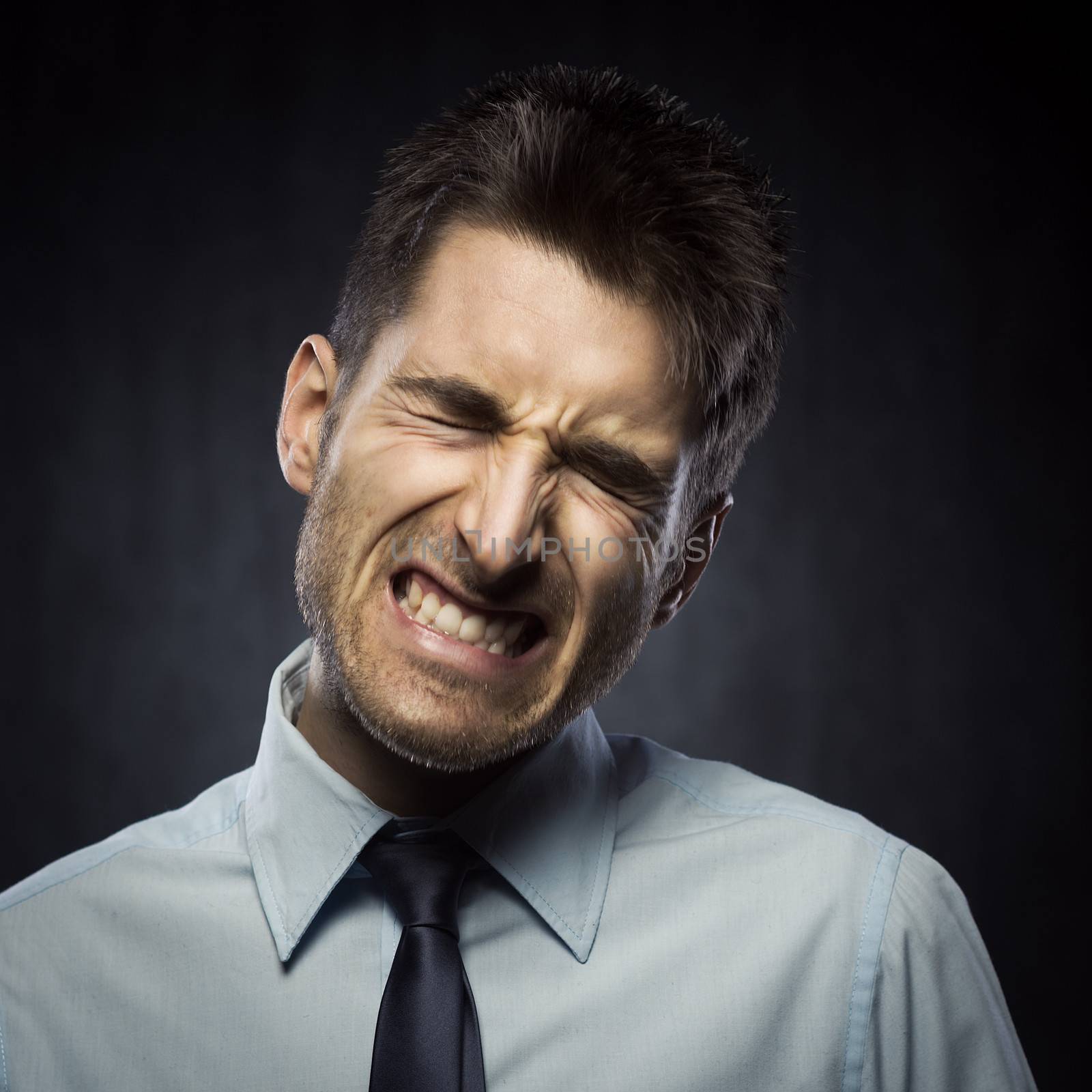 Furious young businessman on dark gray background.