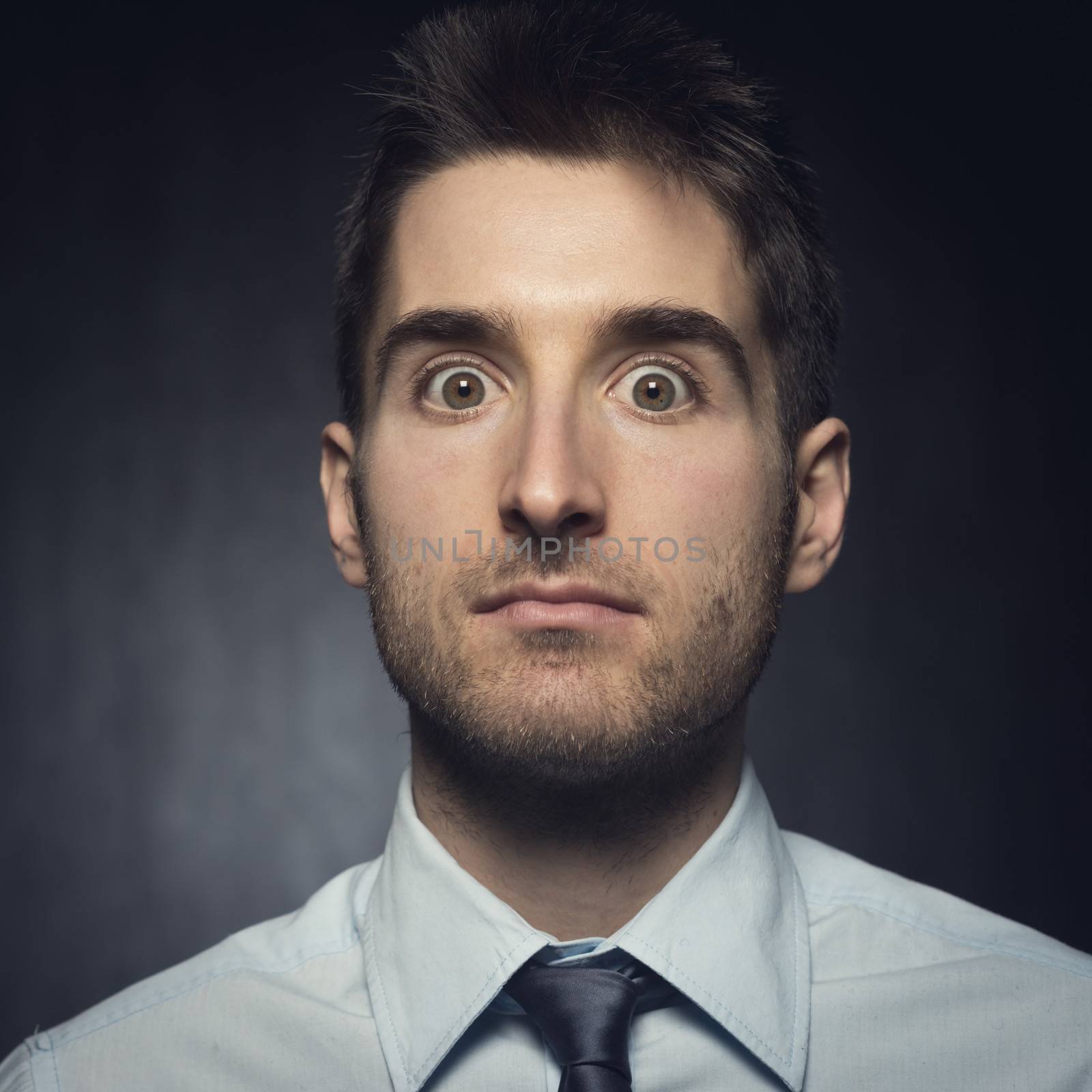 Young elegant man looking at camera expressing surprise.