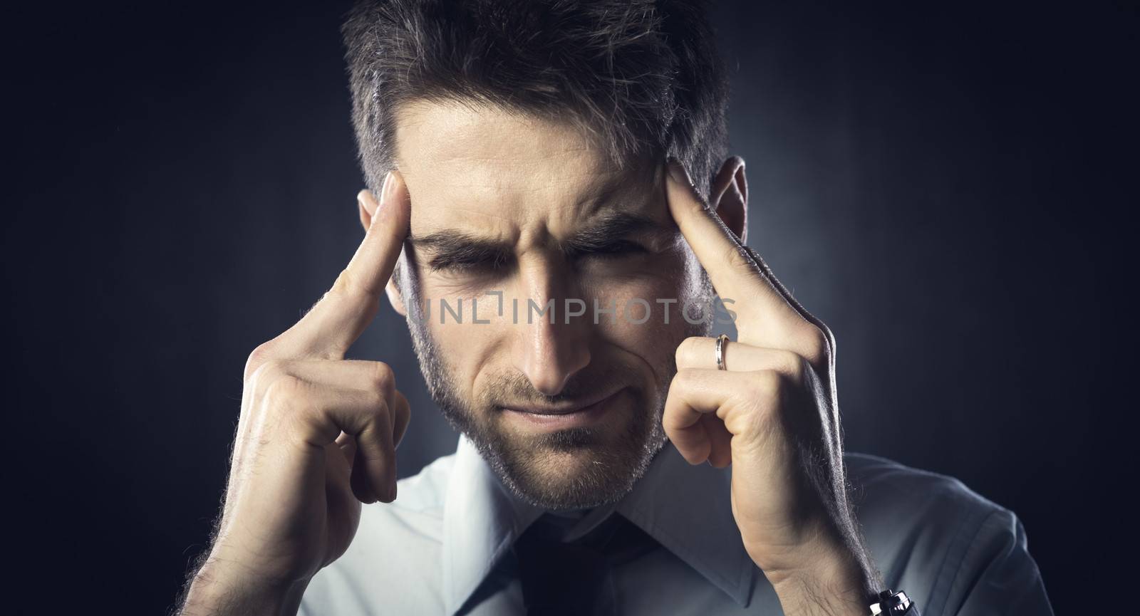Exhausted young businessman with headache touching his head.