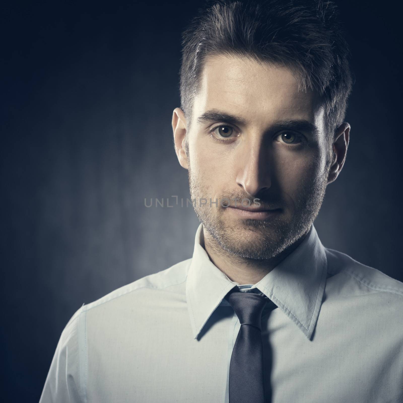 Confident businessman looking at camera on dark background.