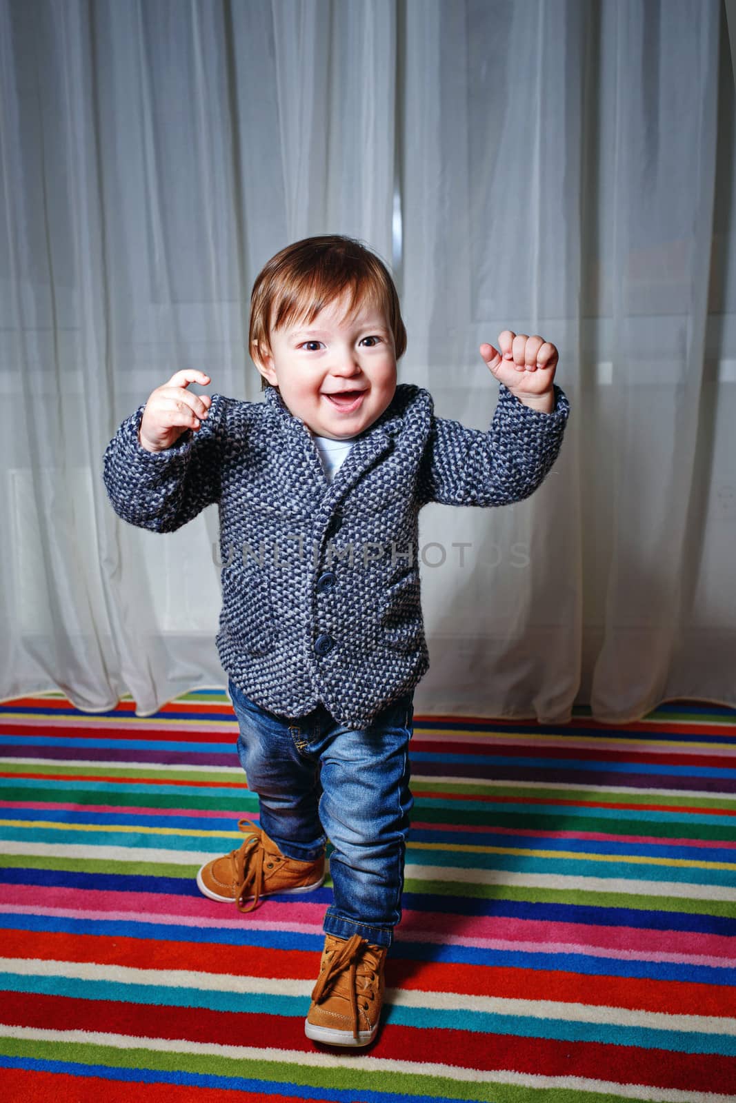 Little boy in a single-breasted jacket and jeans held up his hands in a moment of joy