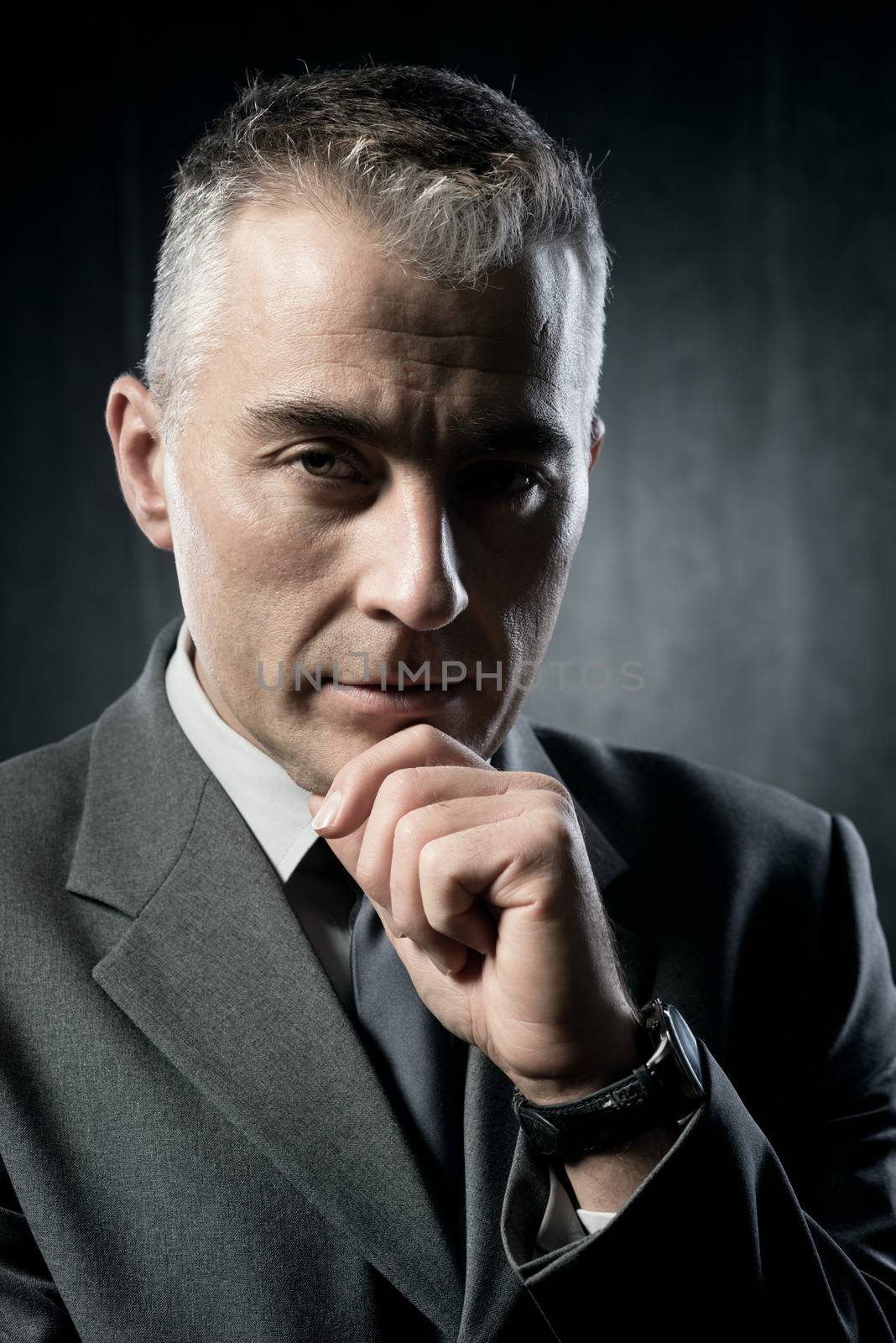 Pensive businessman with hand on chin on dark background.