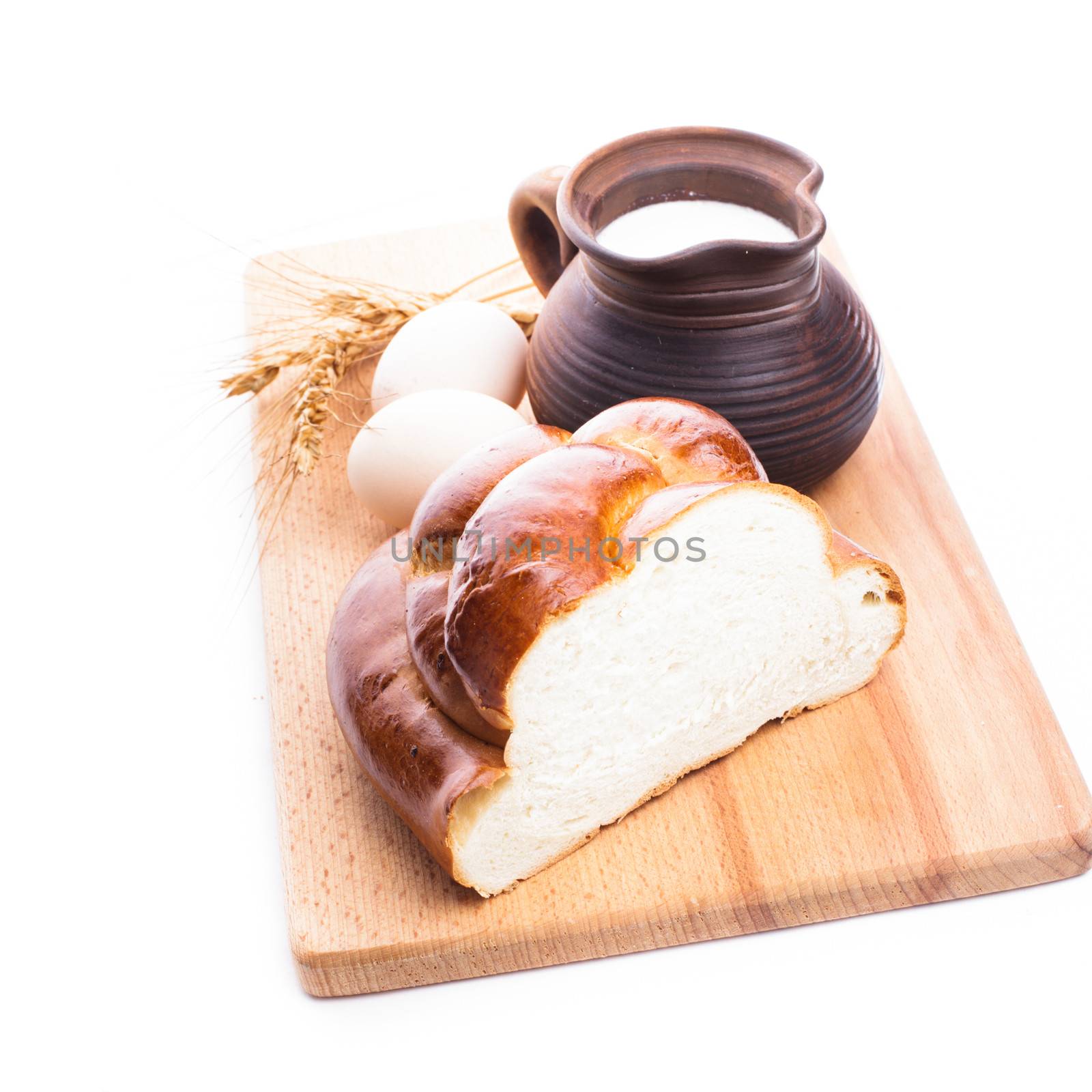 Fresh loaf of challah with milk and eggs on the wooden board