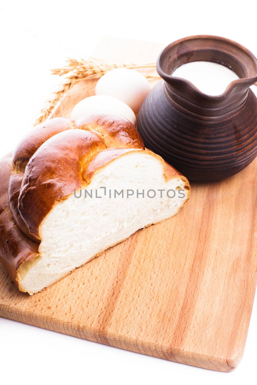 Fresh loaf of challah with milk and eggs on the wooden board