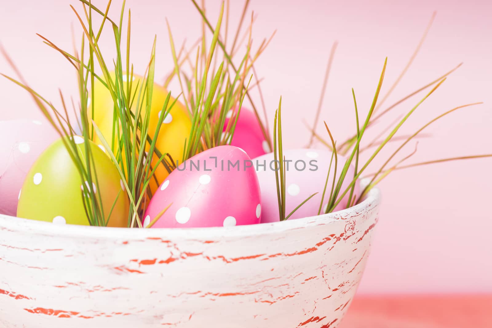 Decorative eggs in pot with grass over pink background. Easter decor.