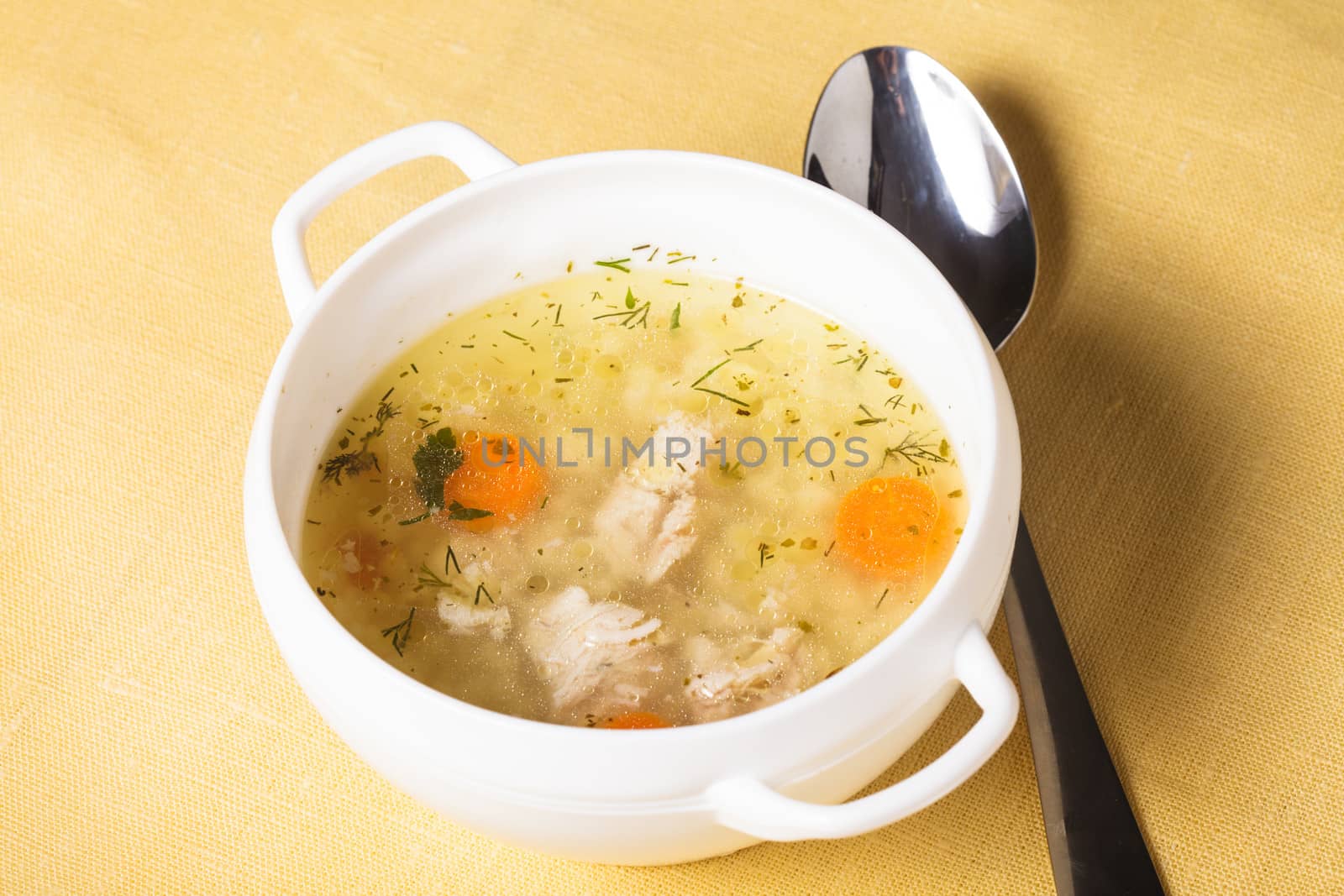 A chicken broth in white ware on the yellow tablecloth