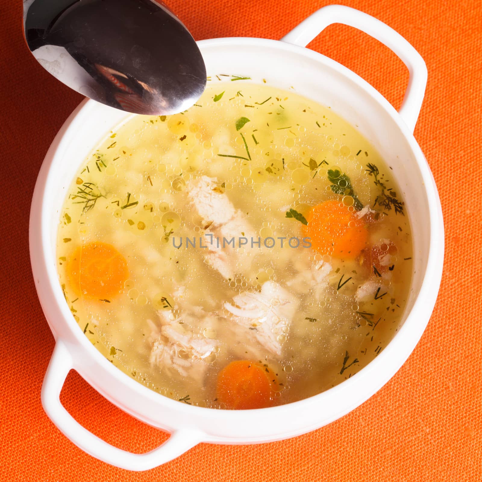 A chicken broth in white ware on the orange tablecloth