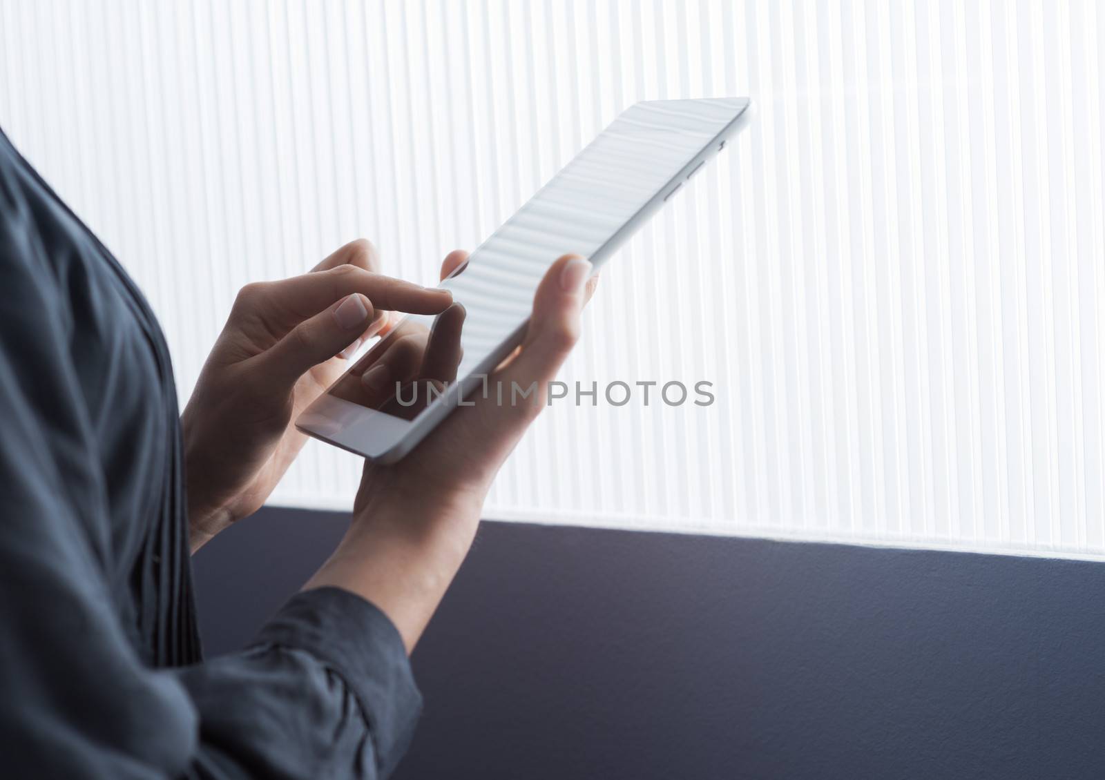 Woman using a digital tablet in front of a window, hands close-up.