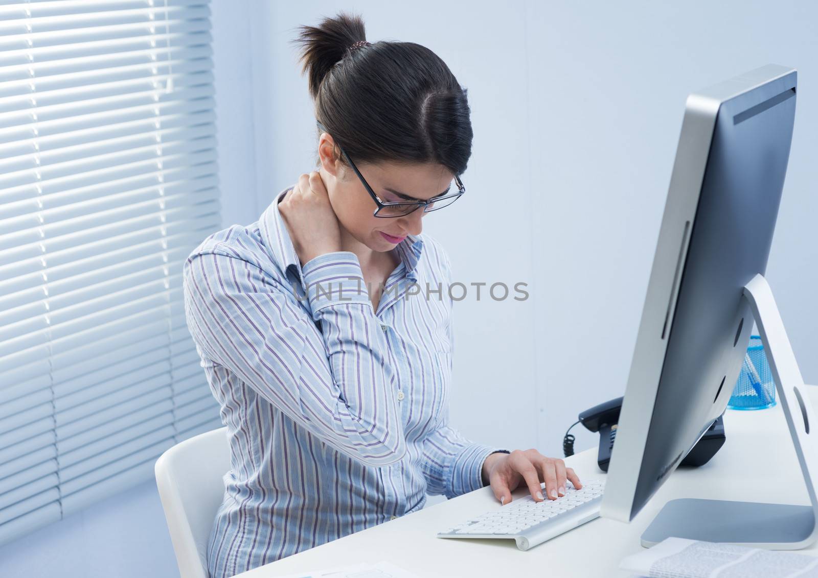 Young office worker with neck pain touching her back.
