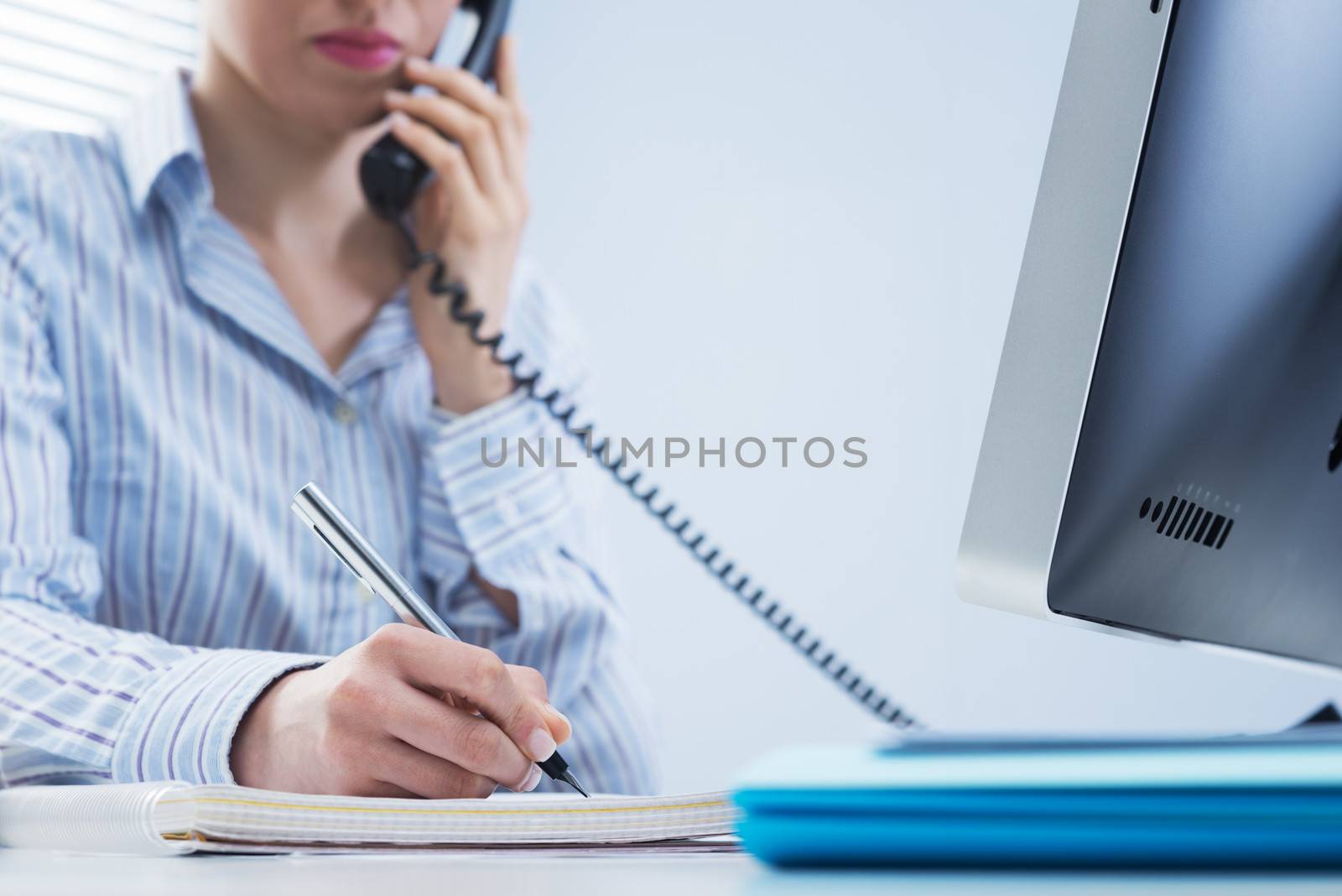 Woman working on the phone and writing down notes at office.