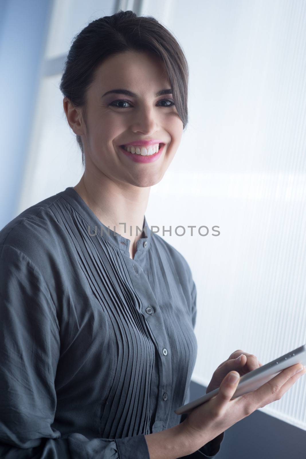 Beautiful woman smiling and using a digital tablet in front of a window.