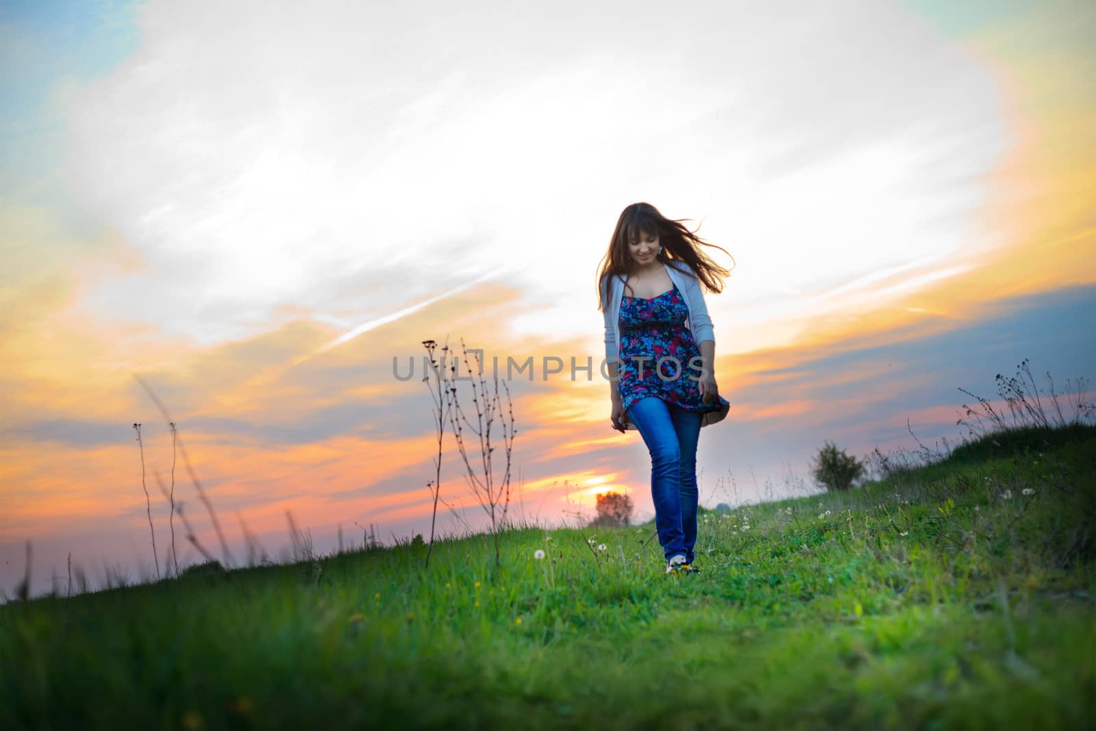 Young woman walks in the evening glow across the meadow