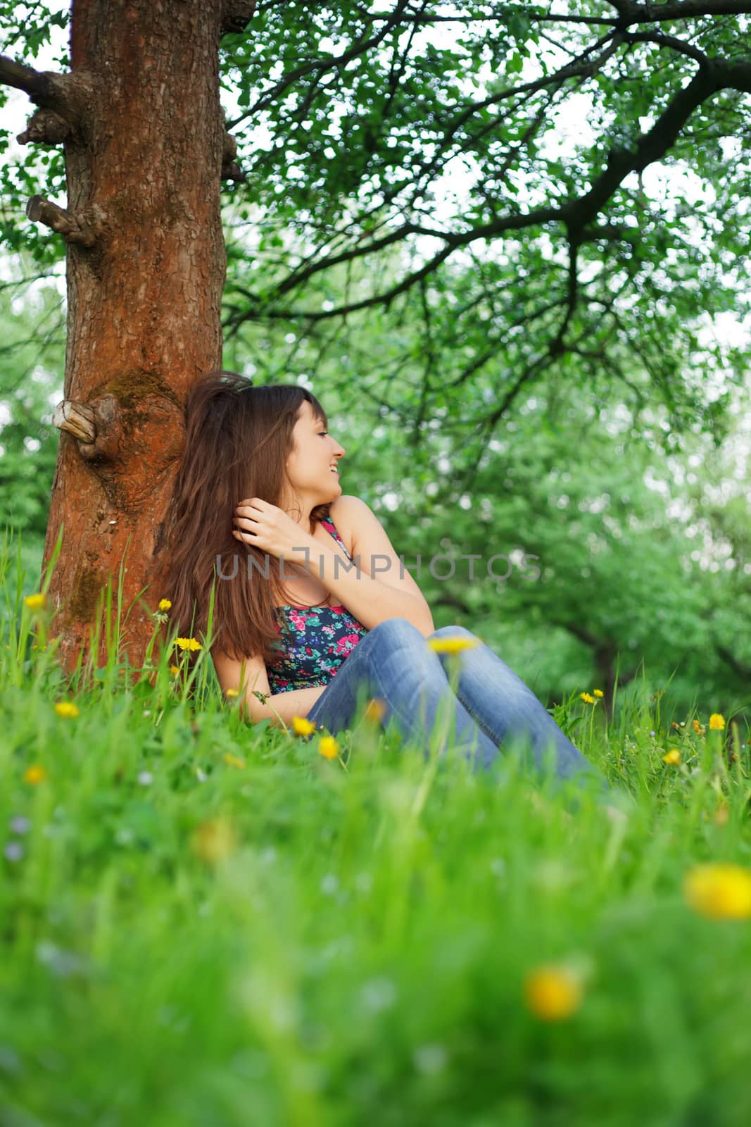 Teenage girl is resting in the park, sitting on the grass. Enjoying the nature.