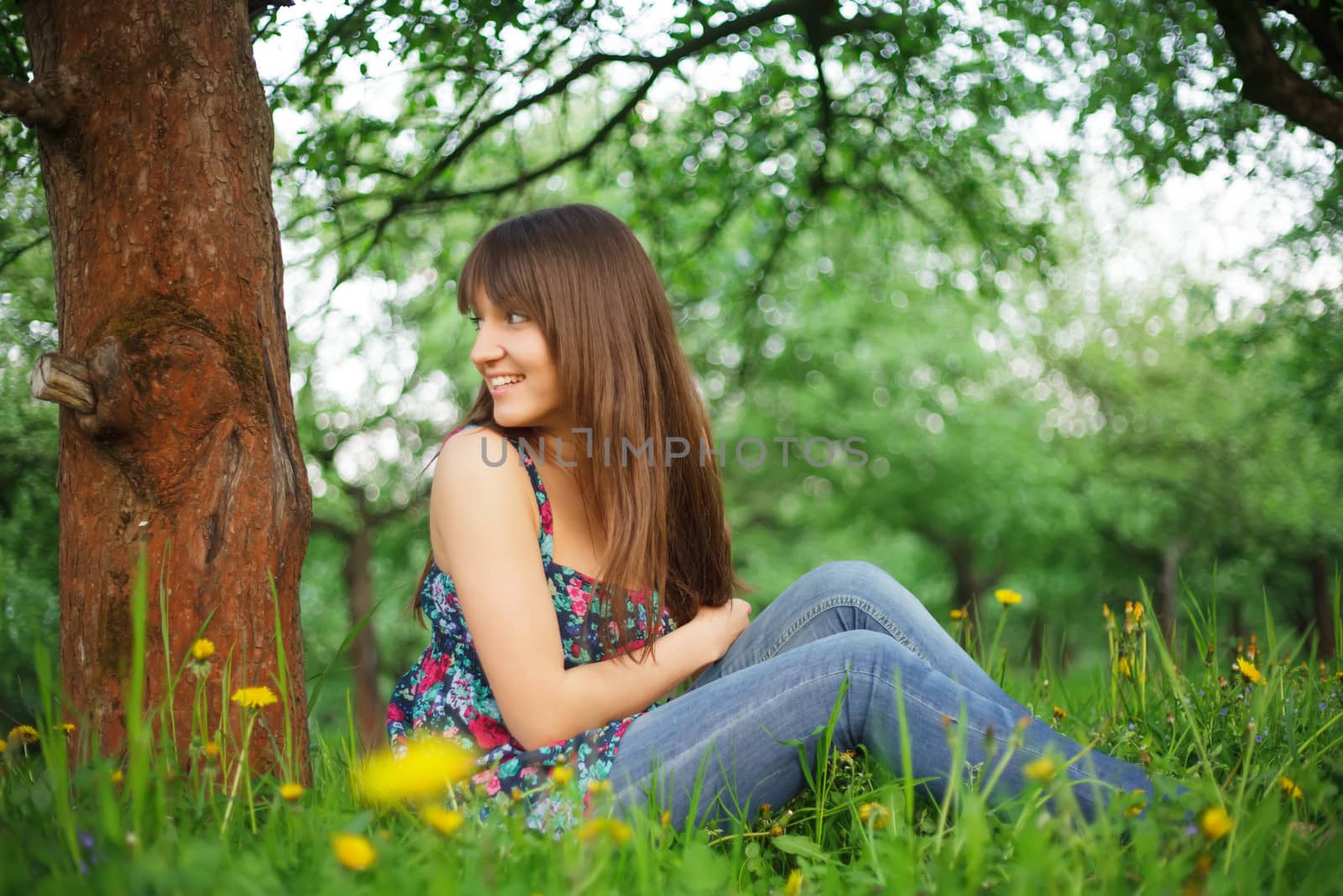 Teenage girl is resting in the park, sitting on the grass. Enjoying the nature.