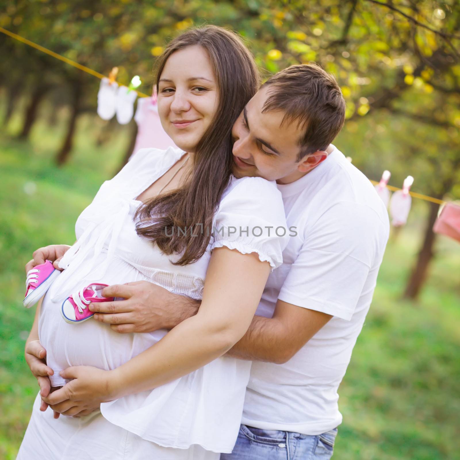 Pregnant couple outdoor in the garden, hold the baby booties