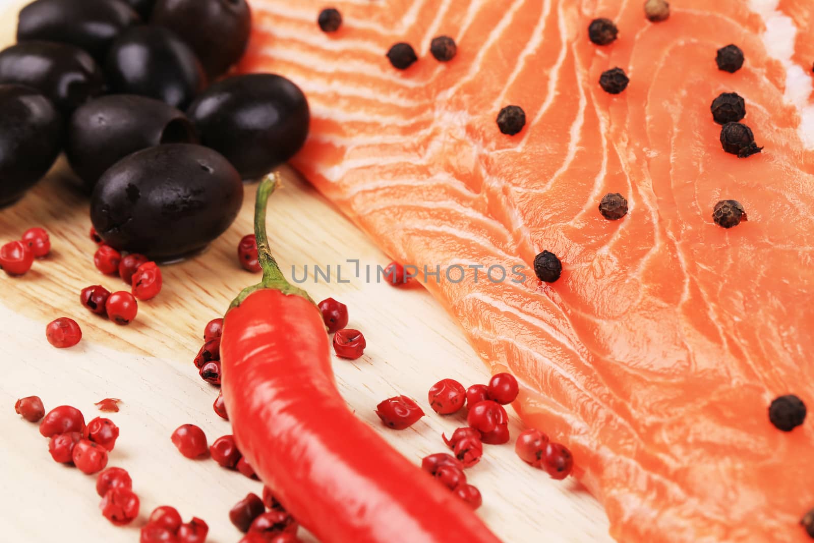 Salmon fillet with olives and red pepper. On a wooden plate.