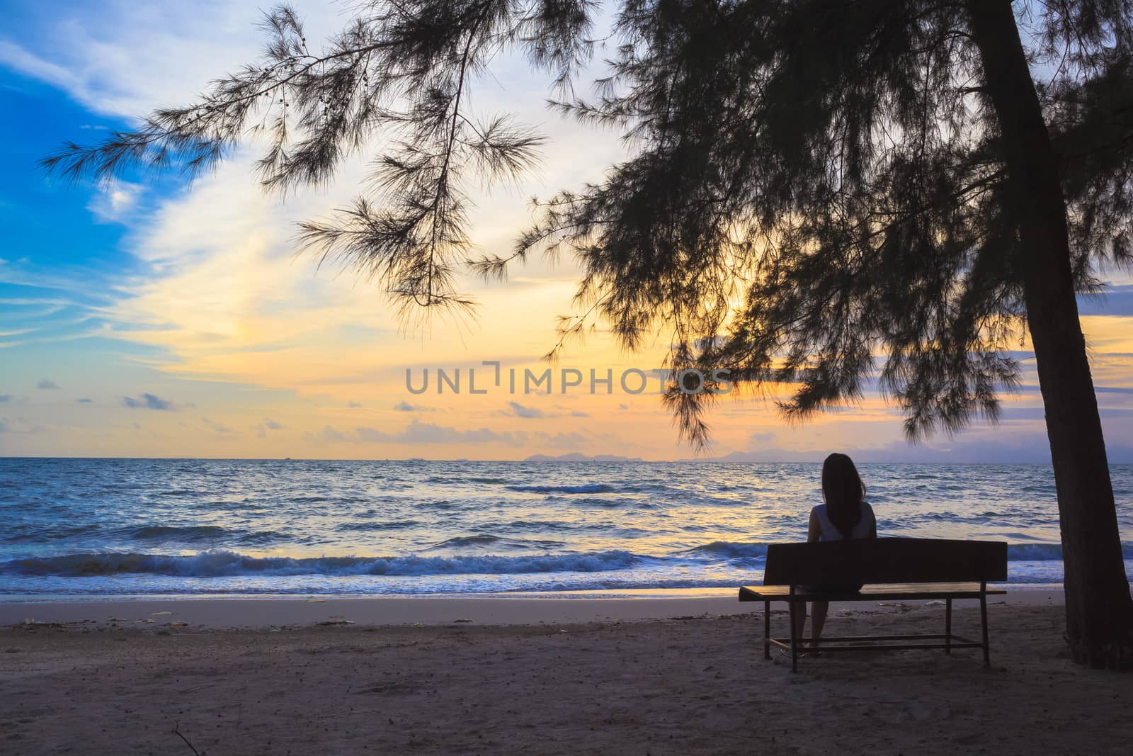 woman sit on chairs under tree on beach at sunset