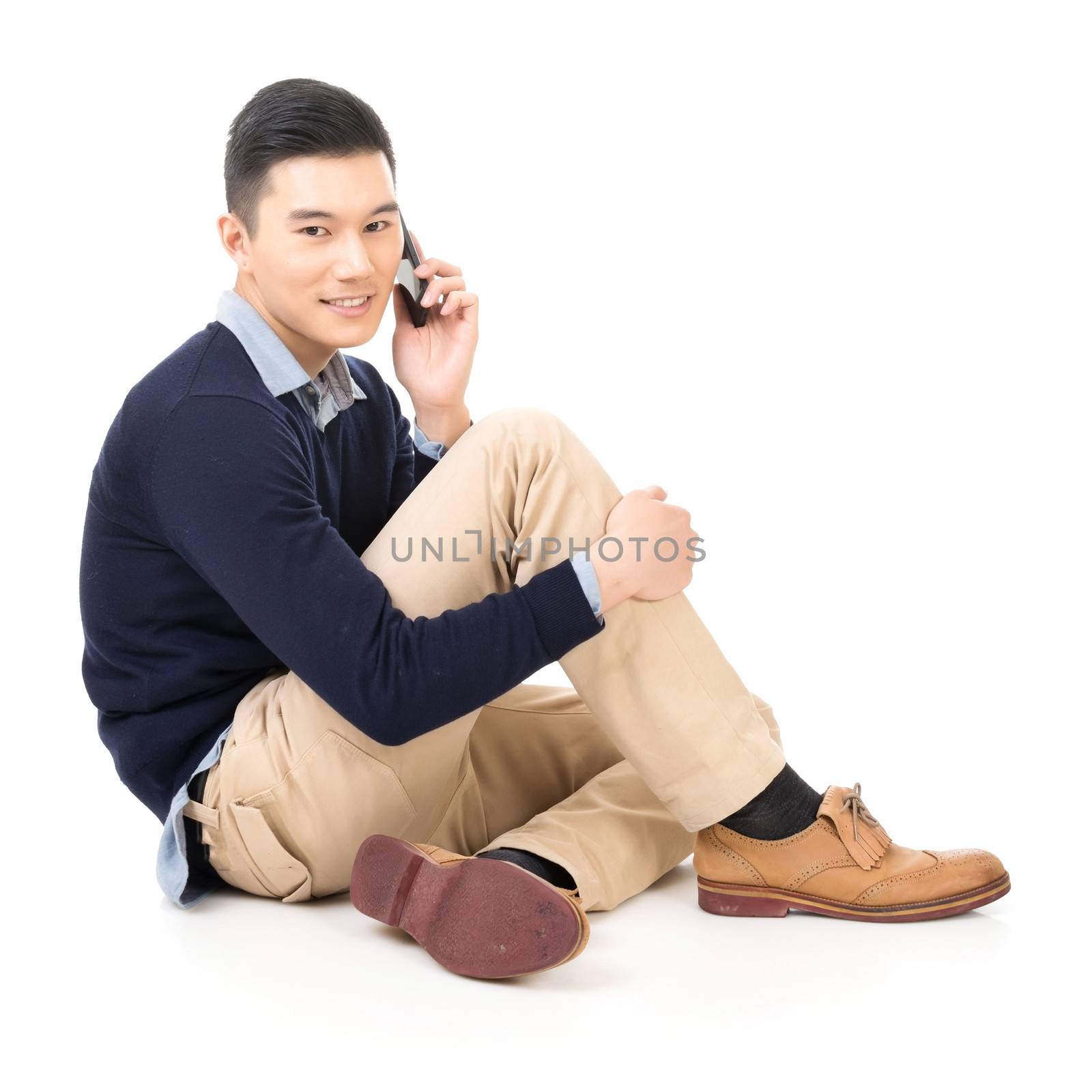 Attractive young man of Asian take a call and sit on ground, full length portrait.