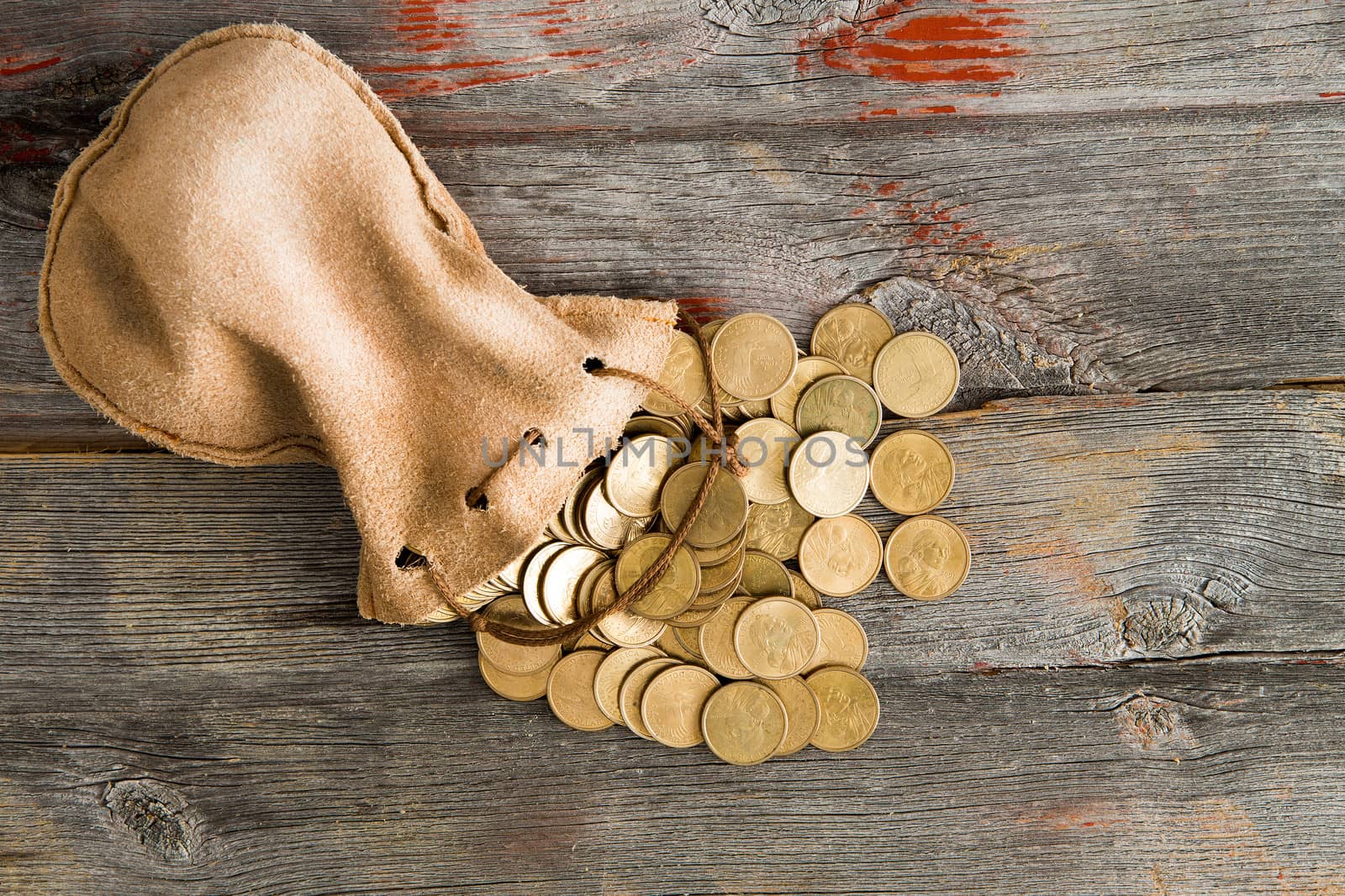 Pile of dollar coins spilling out of a drawstring pouch onto a rustic old weathered wooden table, view from above with copyspace