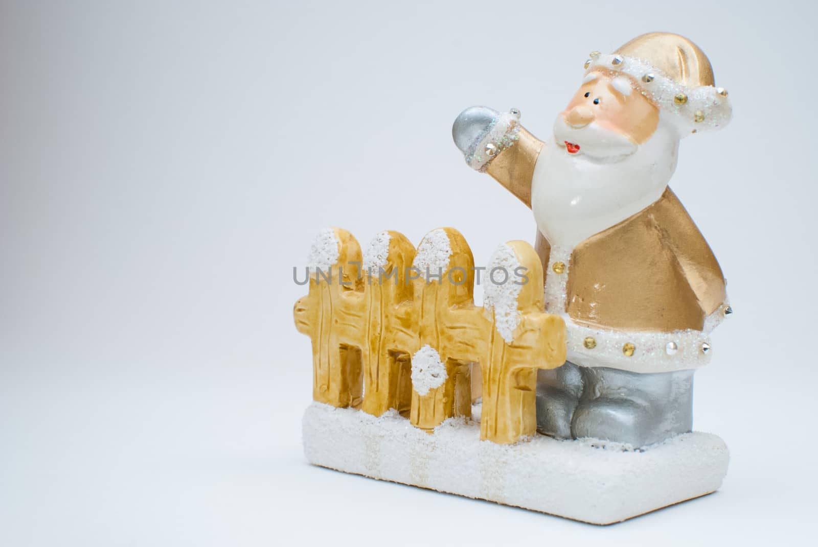 Golden old time Santa Claus figurine standing behind garden fence and waving with one hand, shot in studio with light background