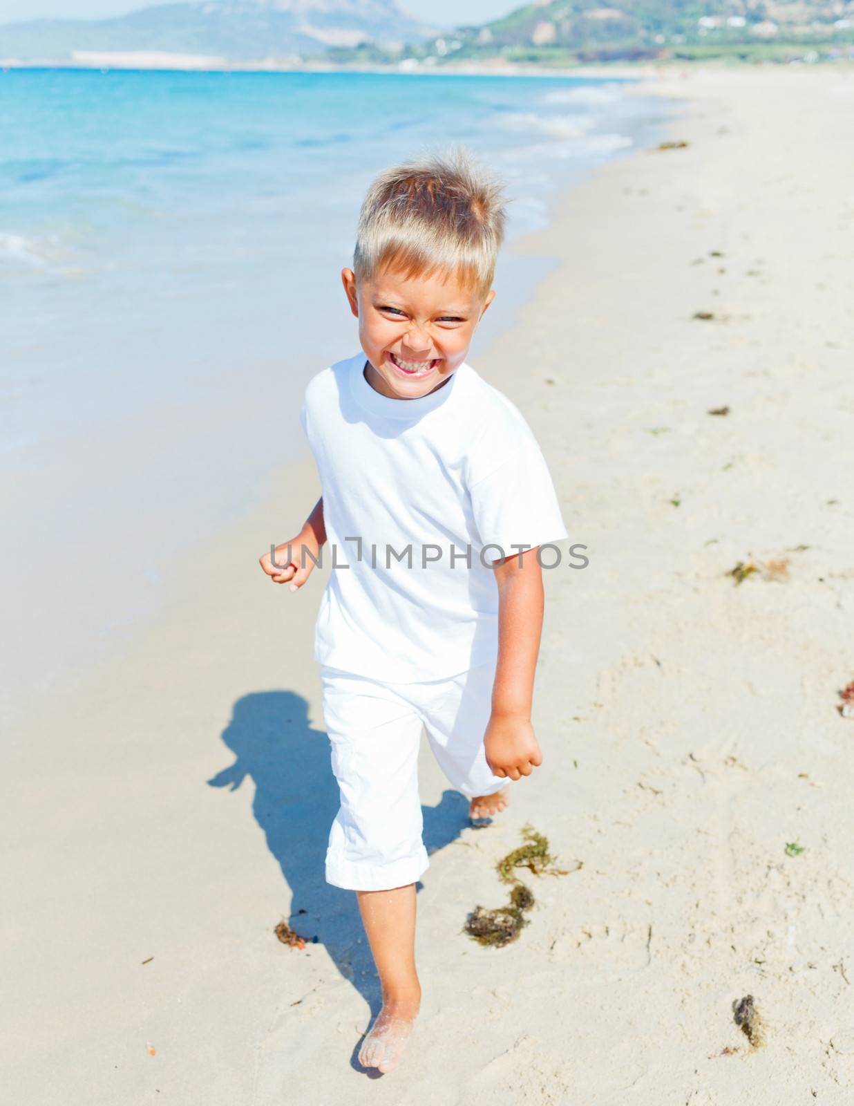 Smiling cute boy runs along the tropical beach.
