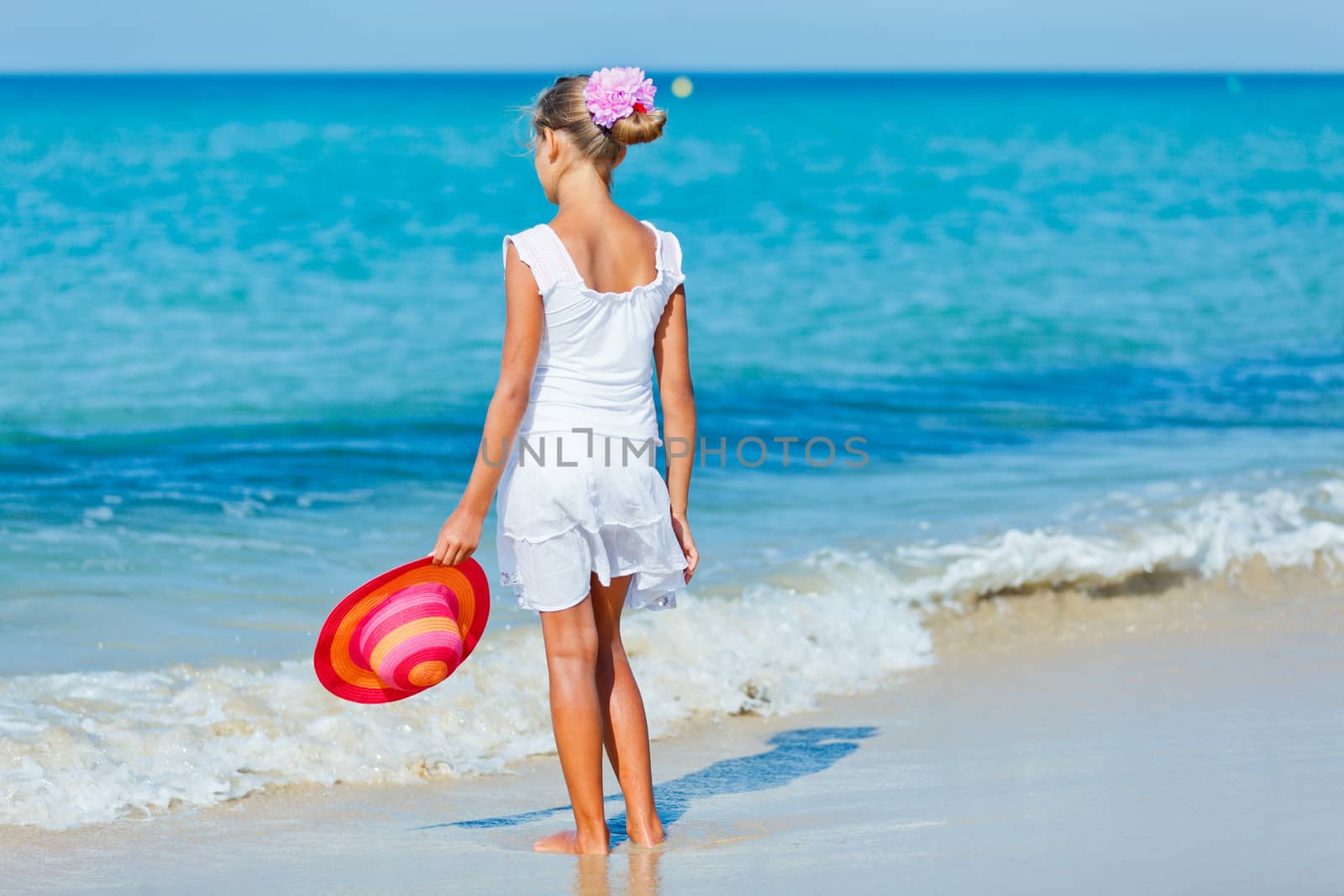 Back view of relaxing beach girl walking with a sun hat at the beach.