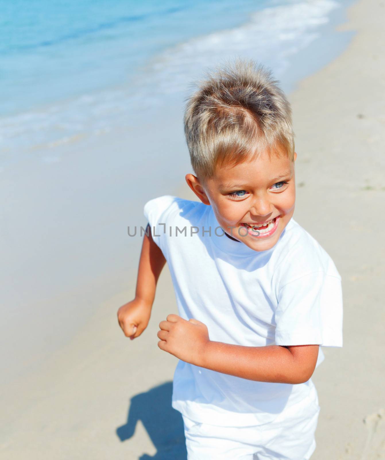 Smiling cute boy runs along the tropical beach.