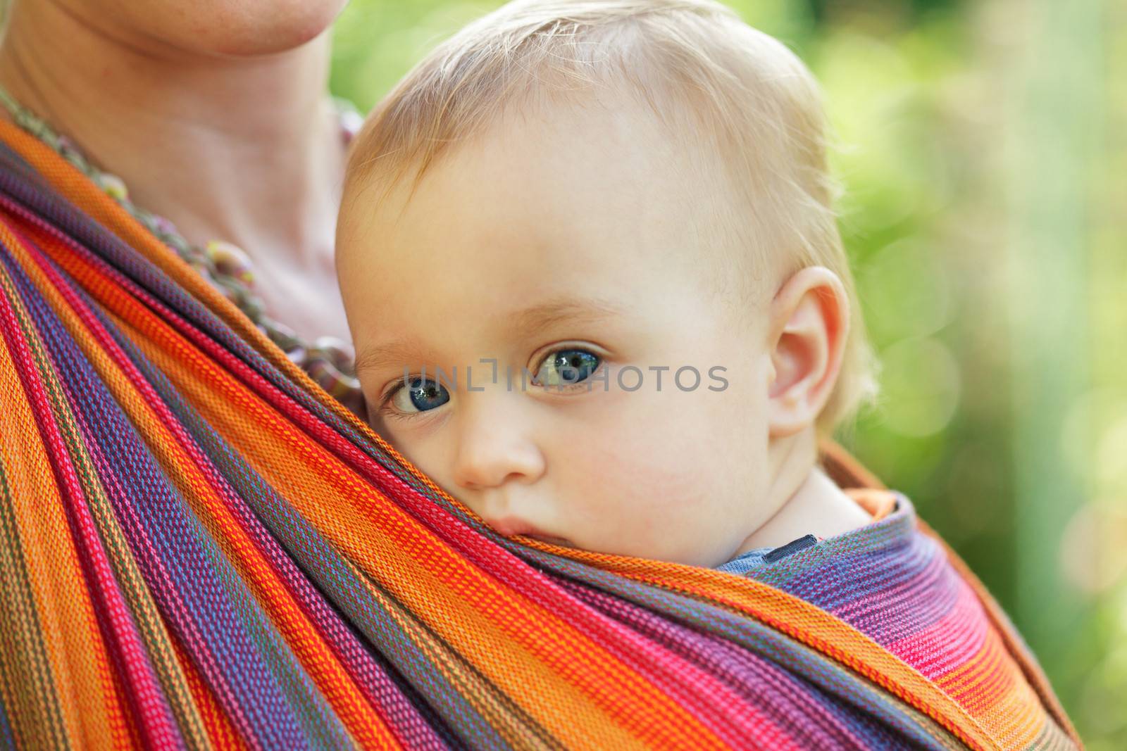 Baby in sling looking outdoor. Mother is carrying her child.