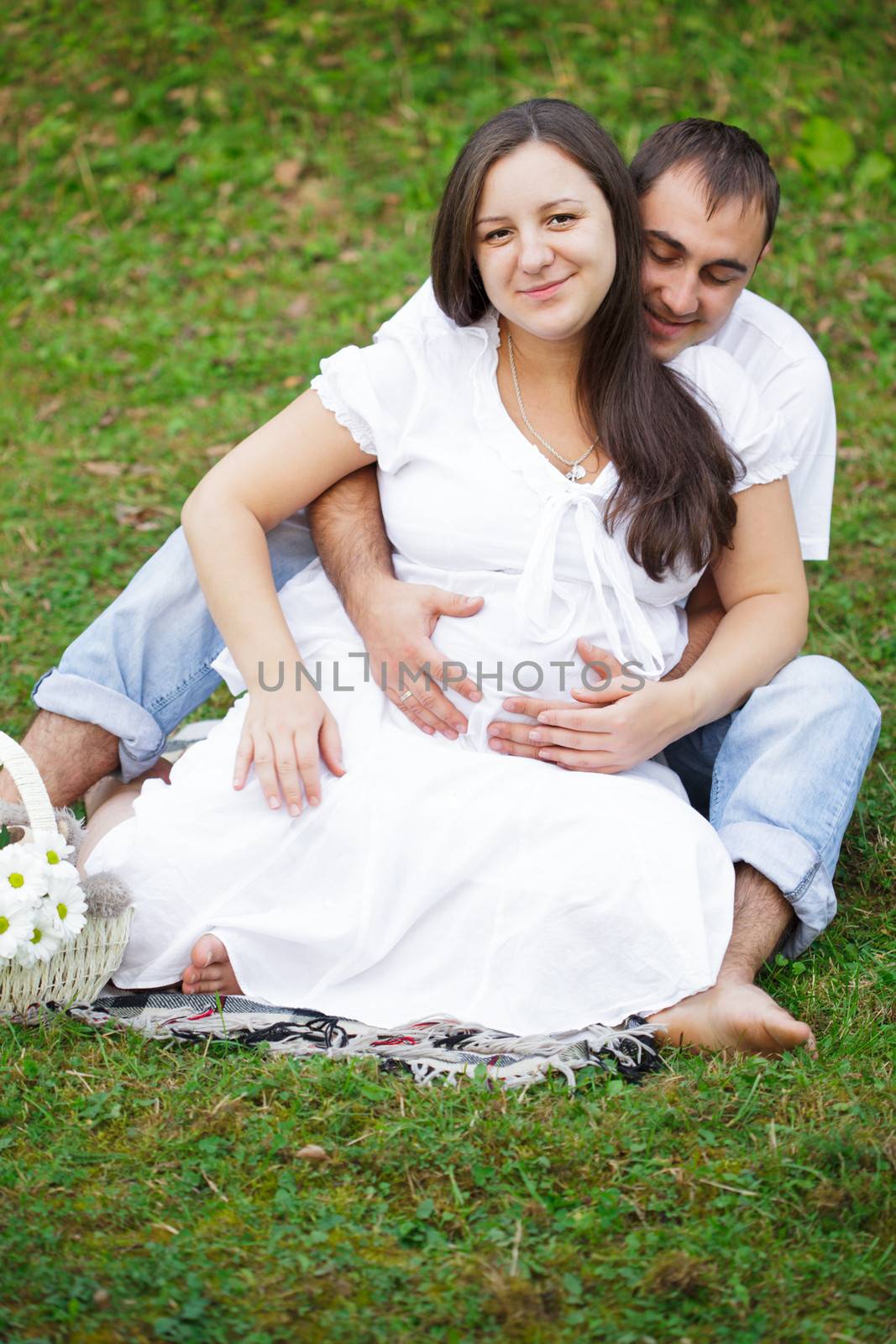 Pregnant couple are sitting on the grass in the park