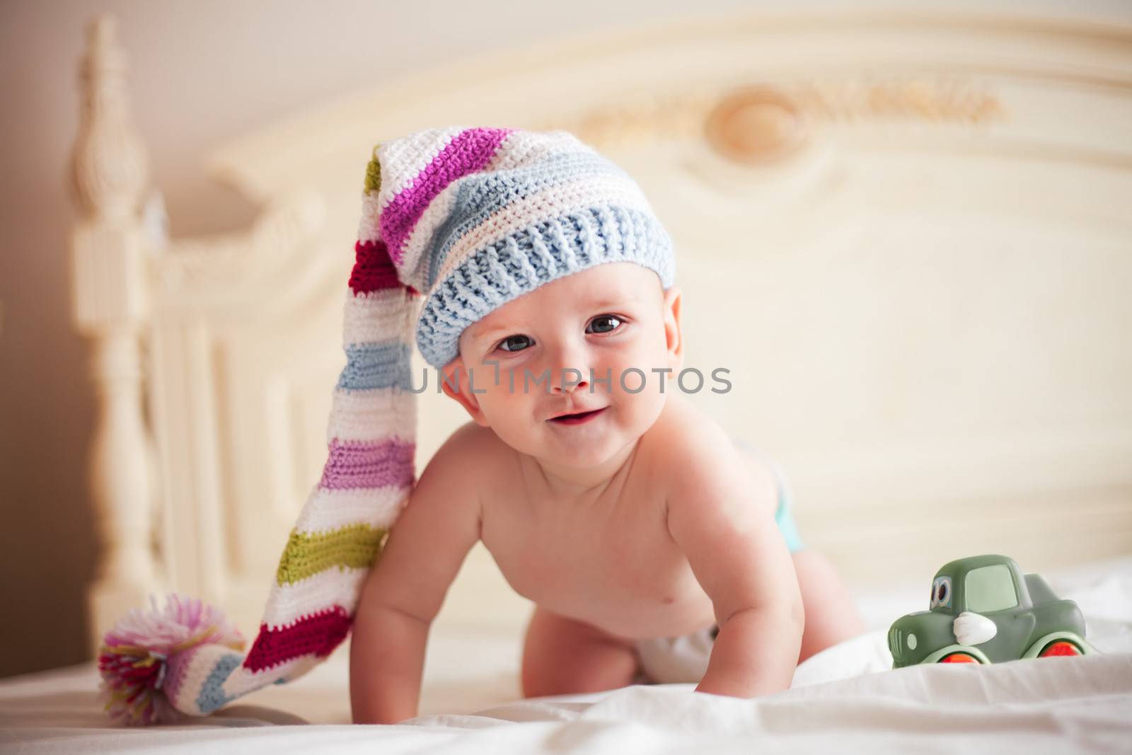 Five-month baby in crochet hat on all fours is smiling
