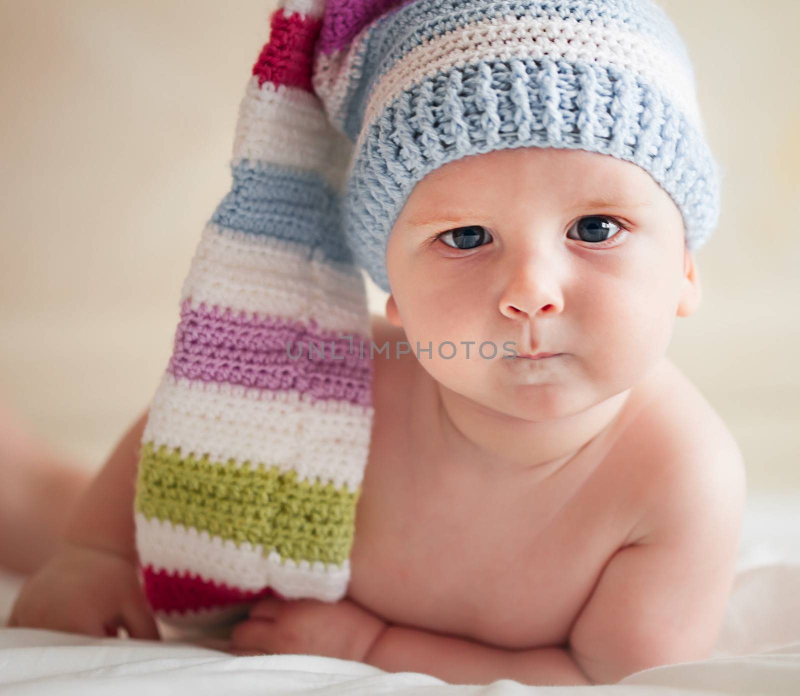 Baby in funny crochet hat lying on the bad