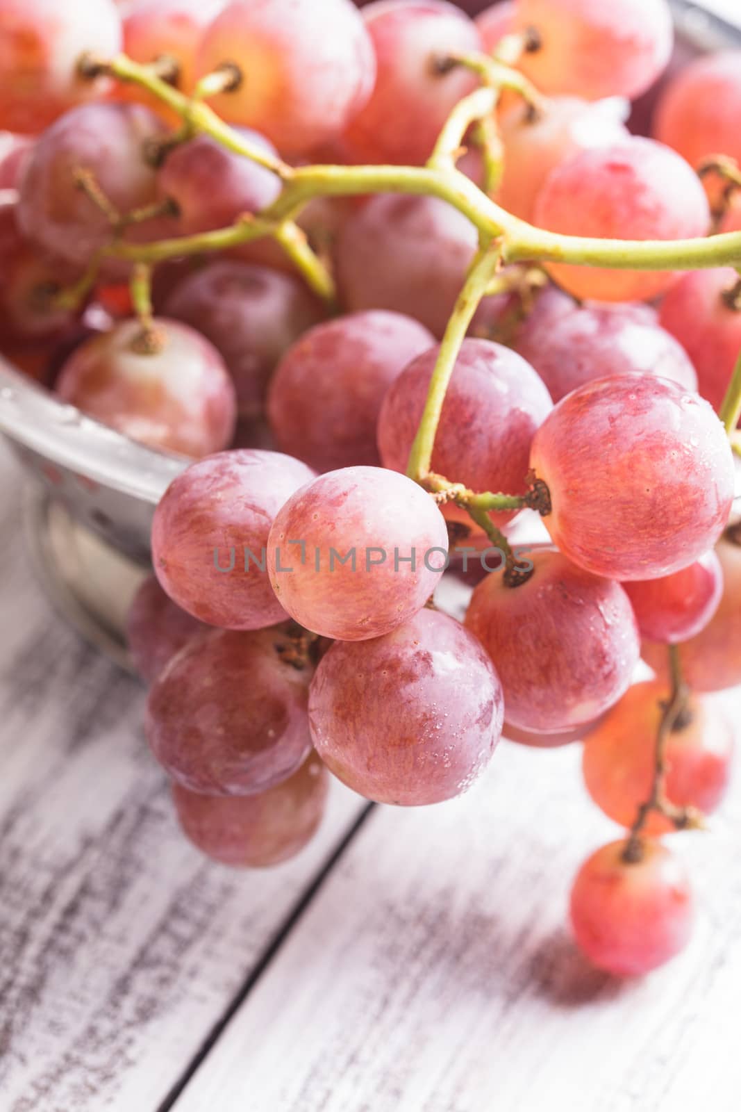 Big red grapes in  colander on the wood background