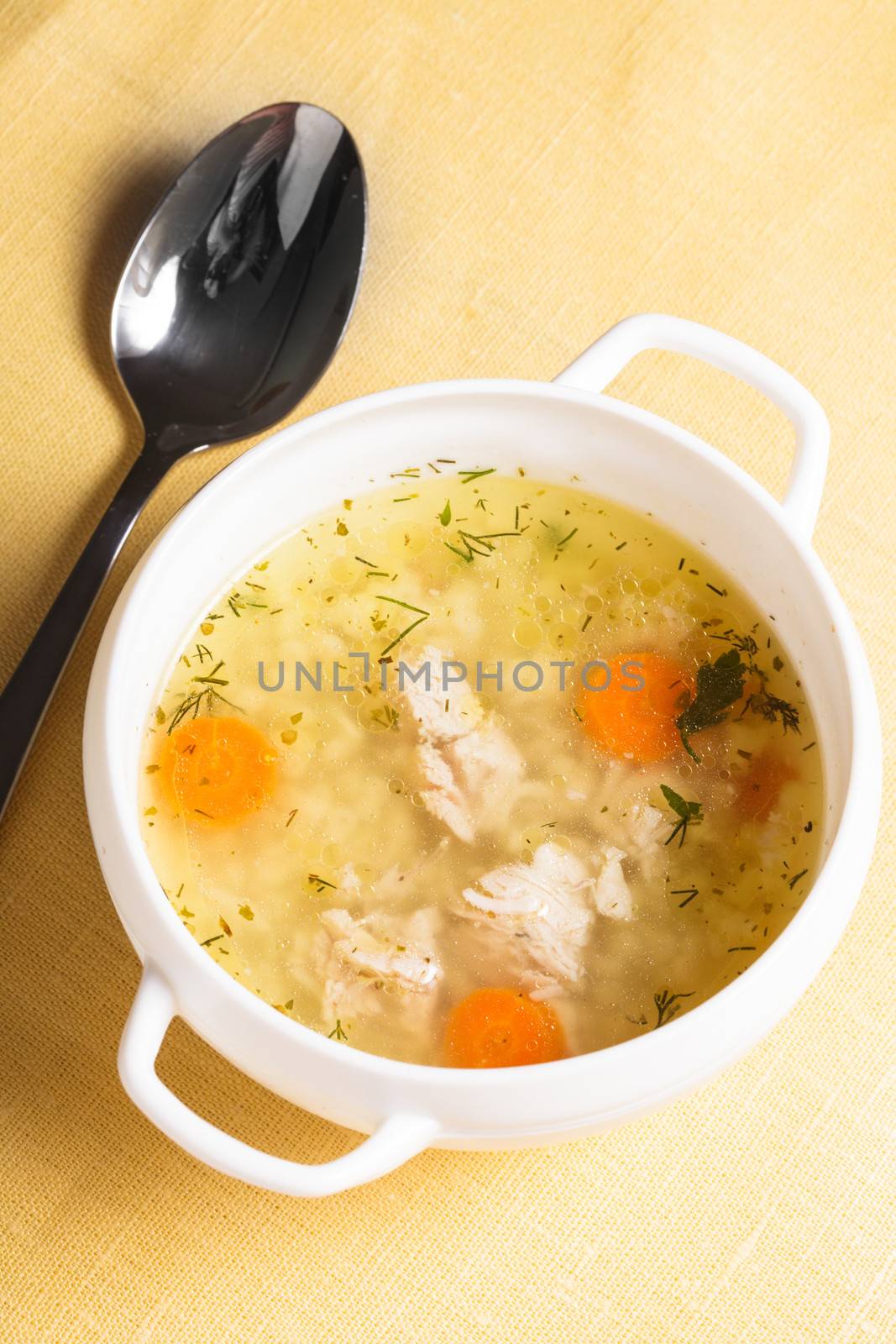 A chicken broth in white ware on the yellow tablecloth