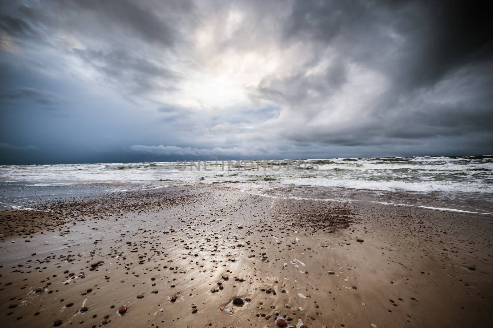 A seaview with the stormy sea, visible small stones and waves, illuminated with dramatic light and dark stormy clouds, ultra wide angle of view.