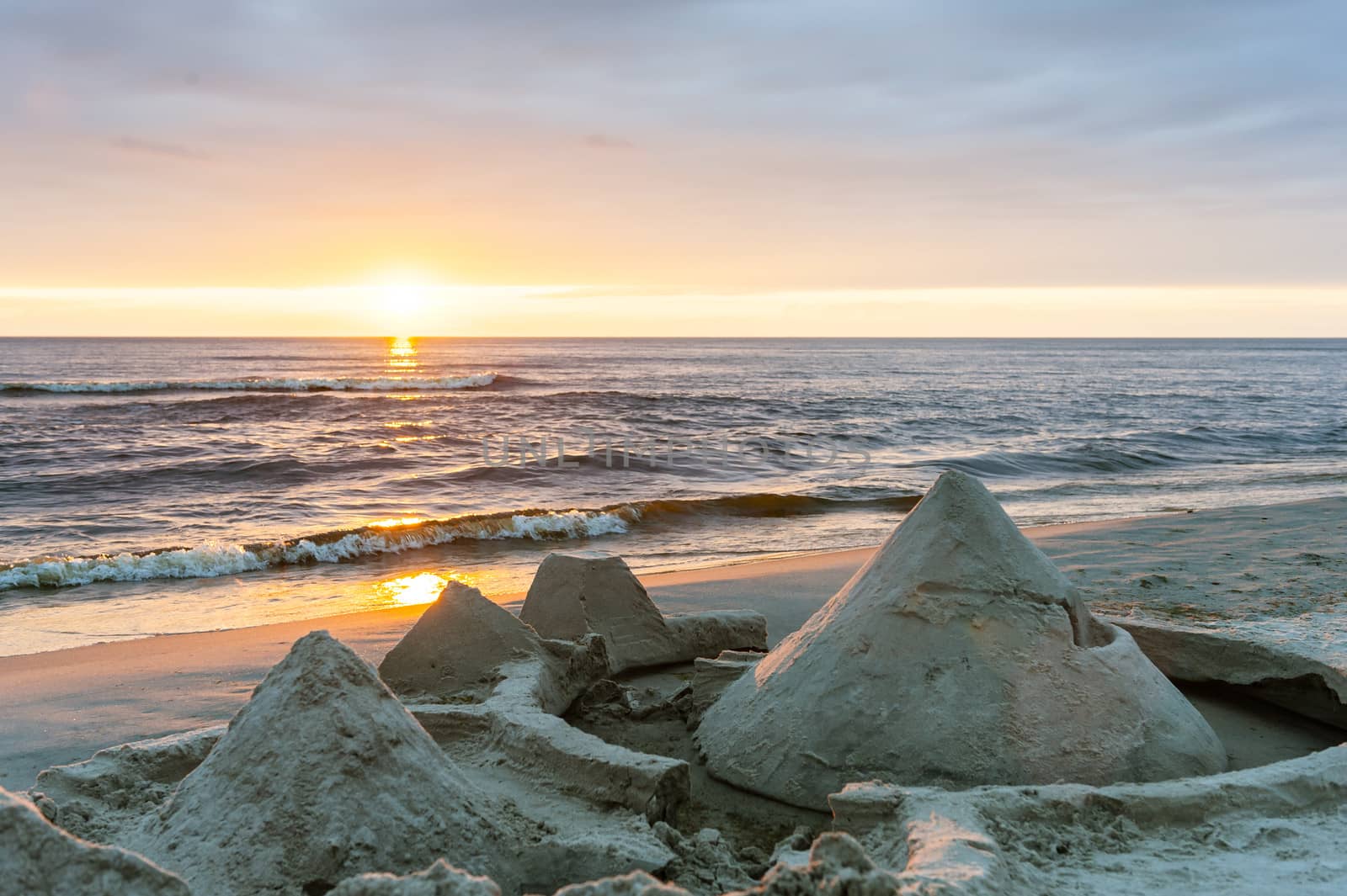 Sandcastles built on the beach by the sea with sunset in the bac by westernstudio