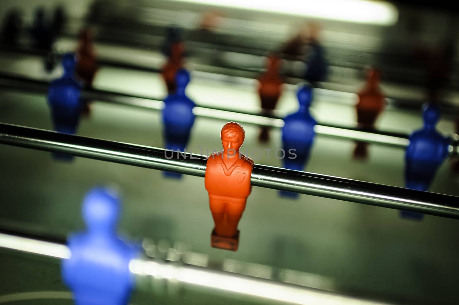 A table football in the pub, visible  figure of a toy mini football player in the red colour and blur other figures of football players (red and blue).