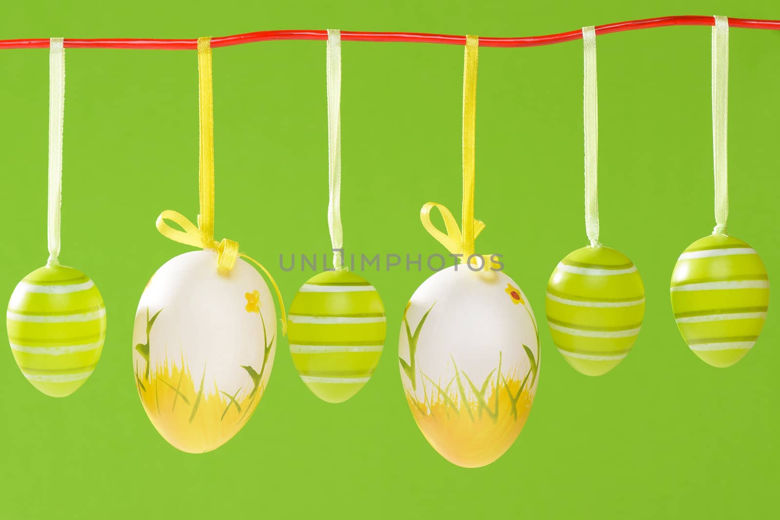 Easter decorated eggs on green backround, eggs in white and green and yellow colours, visible red string.