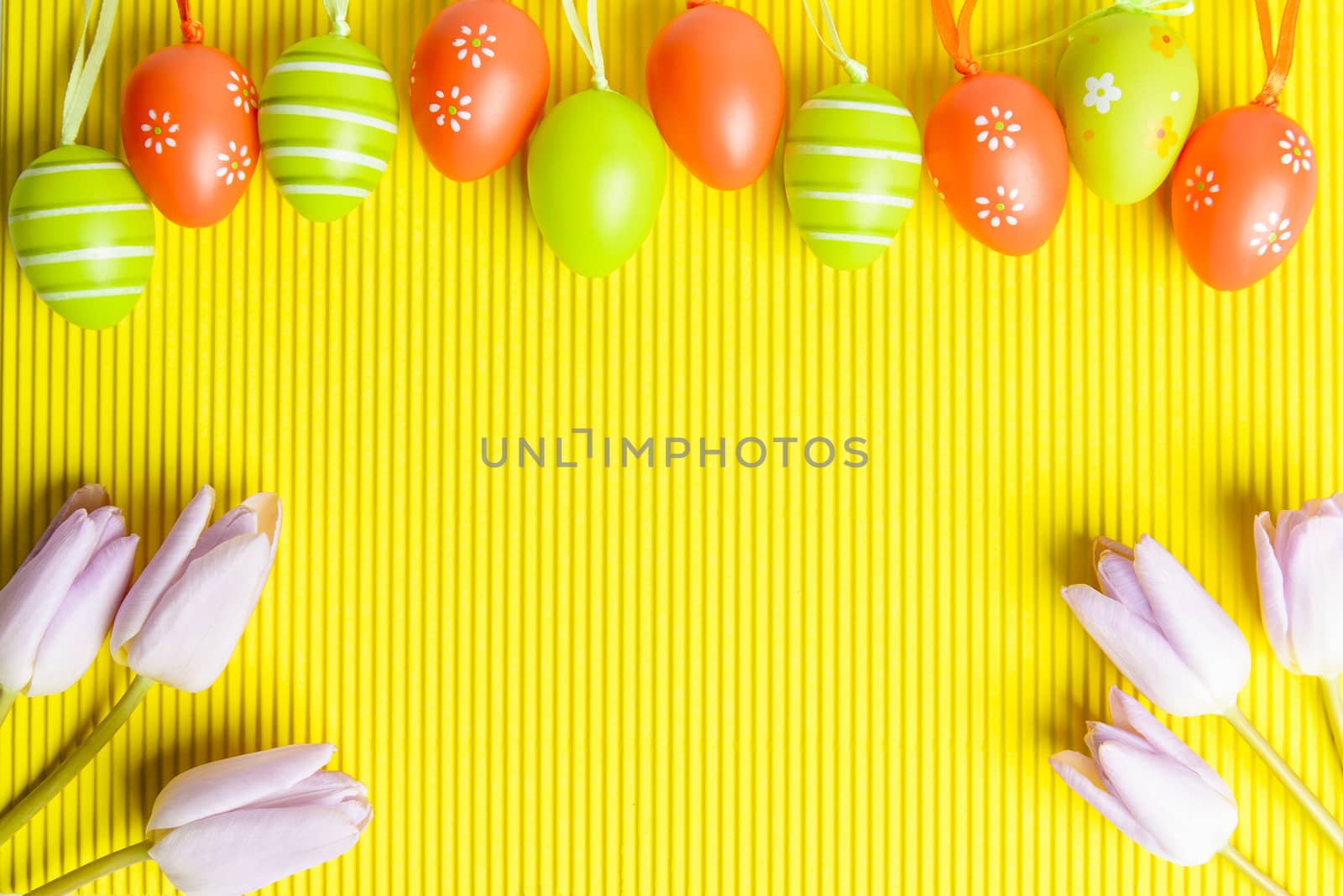 Easter arrangement on yellow background, visible orange and green  decorated eggs and pink tulips in right and left corner, space for text provided.