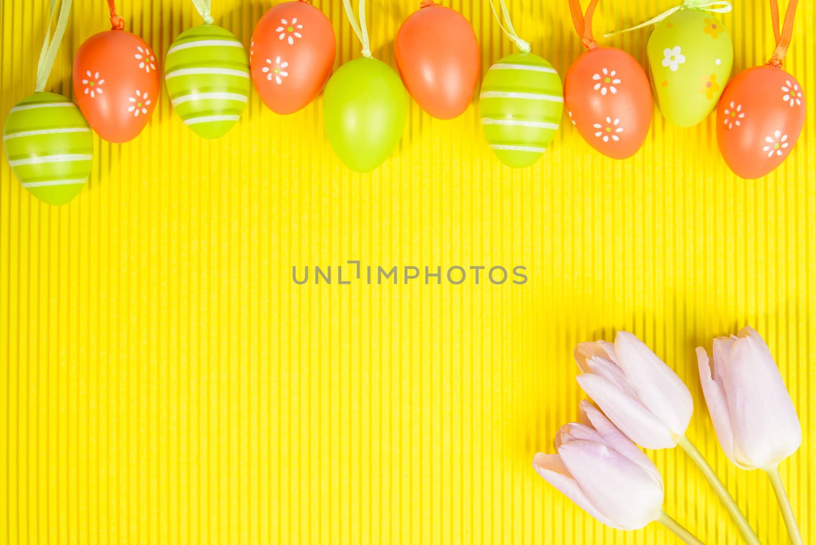 Easter arrangement on yellow background, visible orange and green  decorated eggs and pink tulips in right corner, space for text provided.