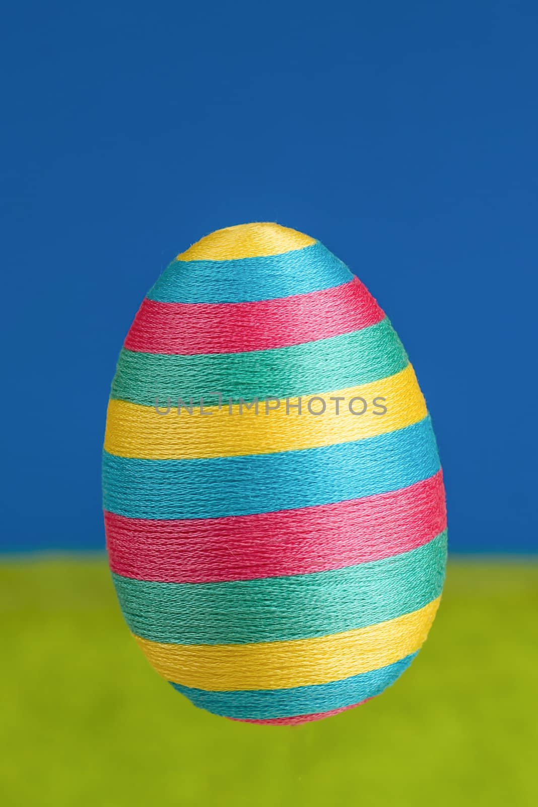 Photo presents big striped rainbow coloured easter egg on green and blue background, space for text provided.