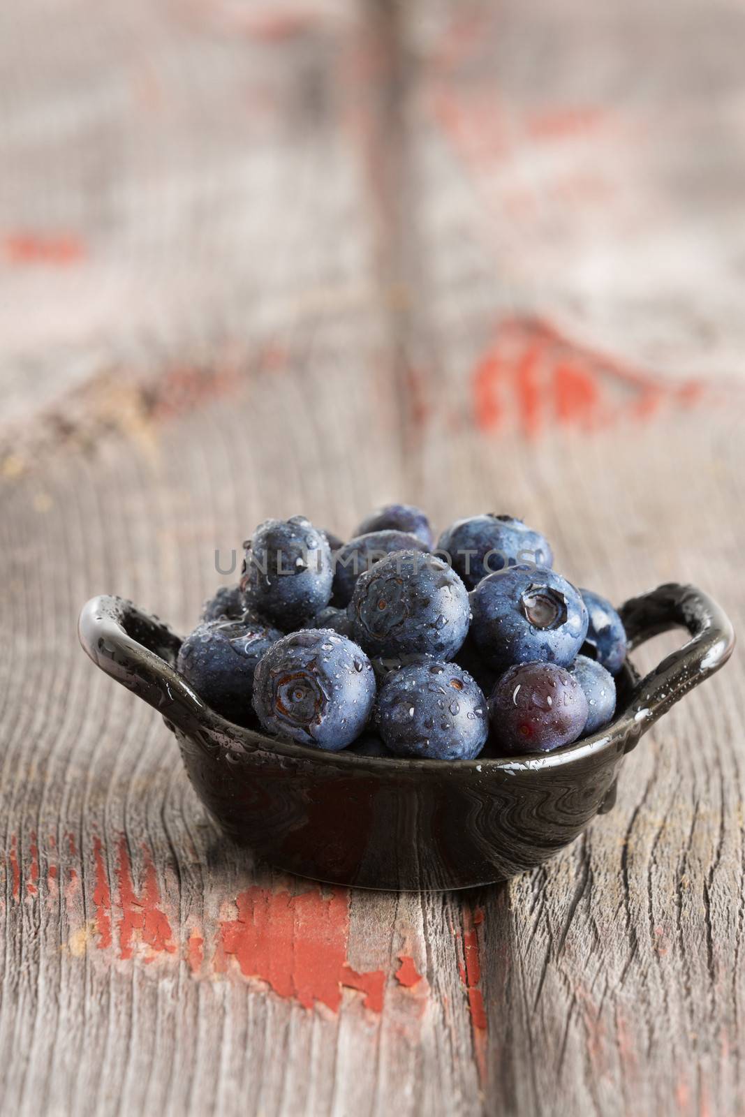 Bowl of fresh ripe autumn blueberries for a healthy diet rich in Vitamin K and antioxidants on old wooden boards in vertical format with shallow dof and copyspace