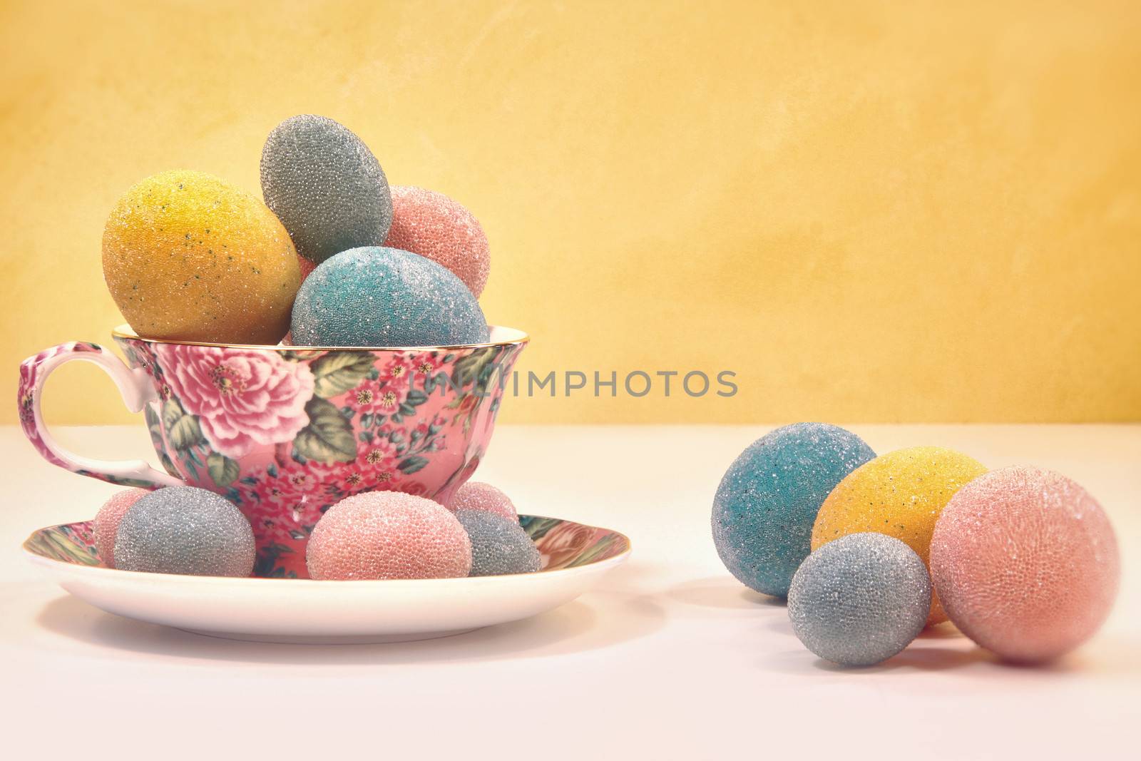 Brightly colored eggs in tea cup on yellow background