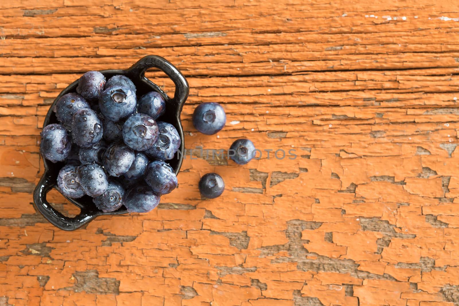 View from above of a ceramic ramekin of fresh ripe blueberries on a grungy wooden table with peeling red paint for a healthy snack rich in vitamins