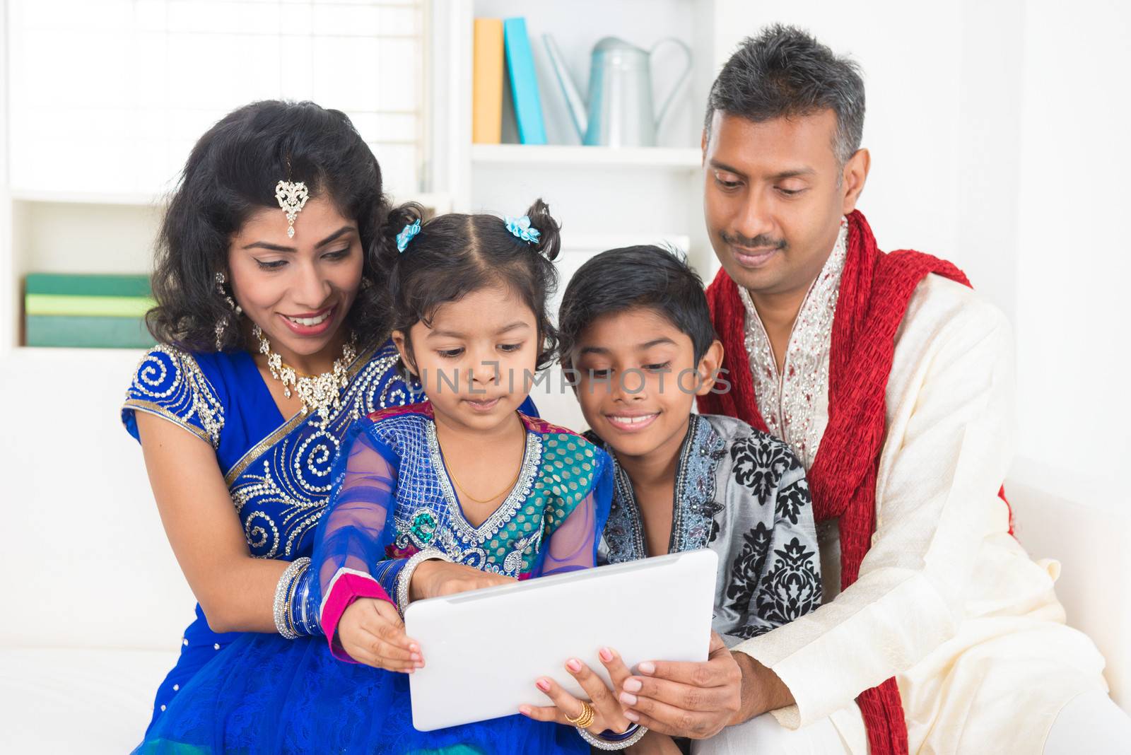 Indian Asian family using tablet pc computer at home. India family living lifestyle in traditional dress. Happy smiling parents and children.