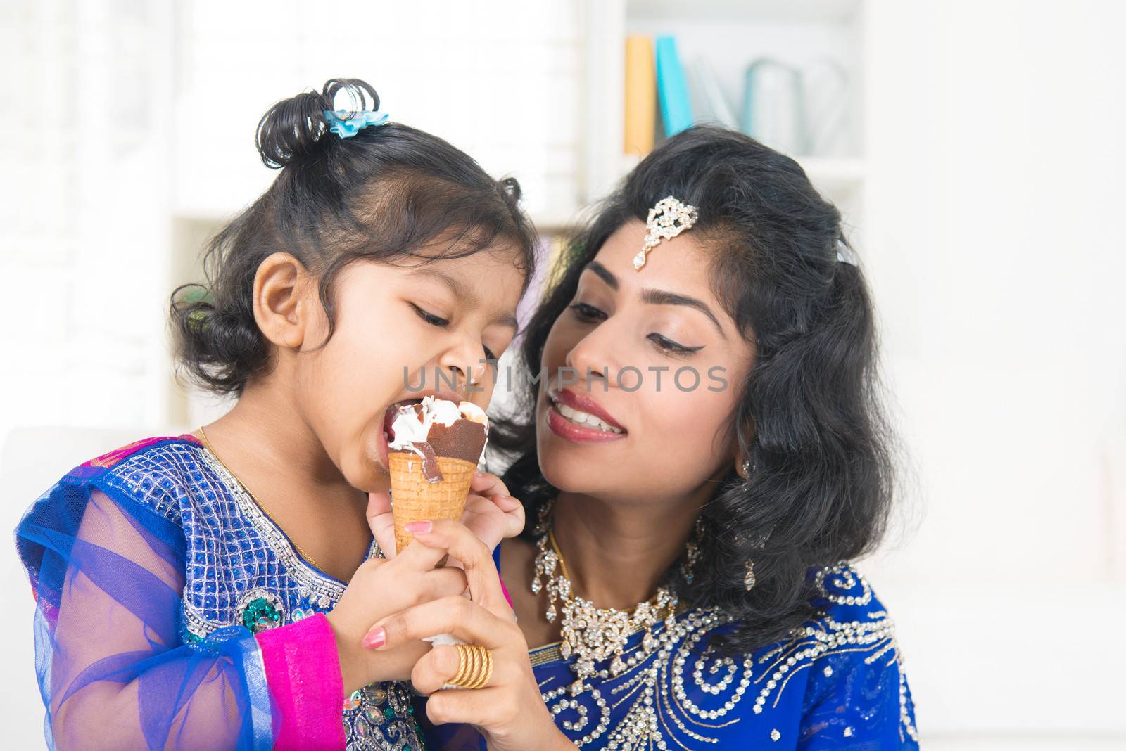 Eating ice-cream. Happy Asian India family sharing ice-cream at home. Beautiful Indian child licking ice-cream cone.