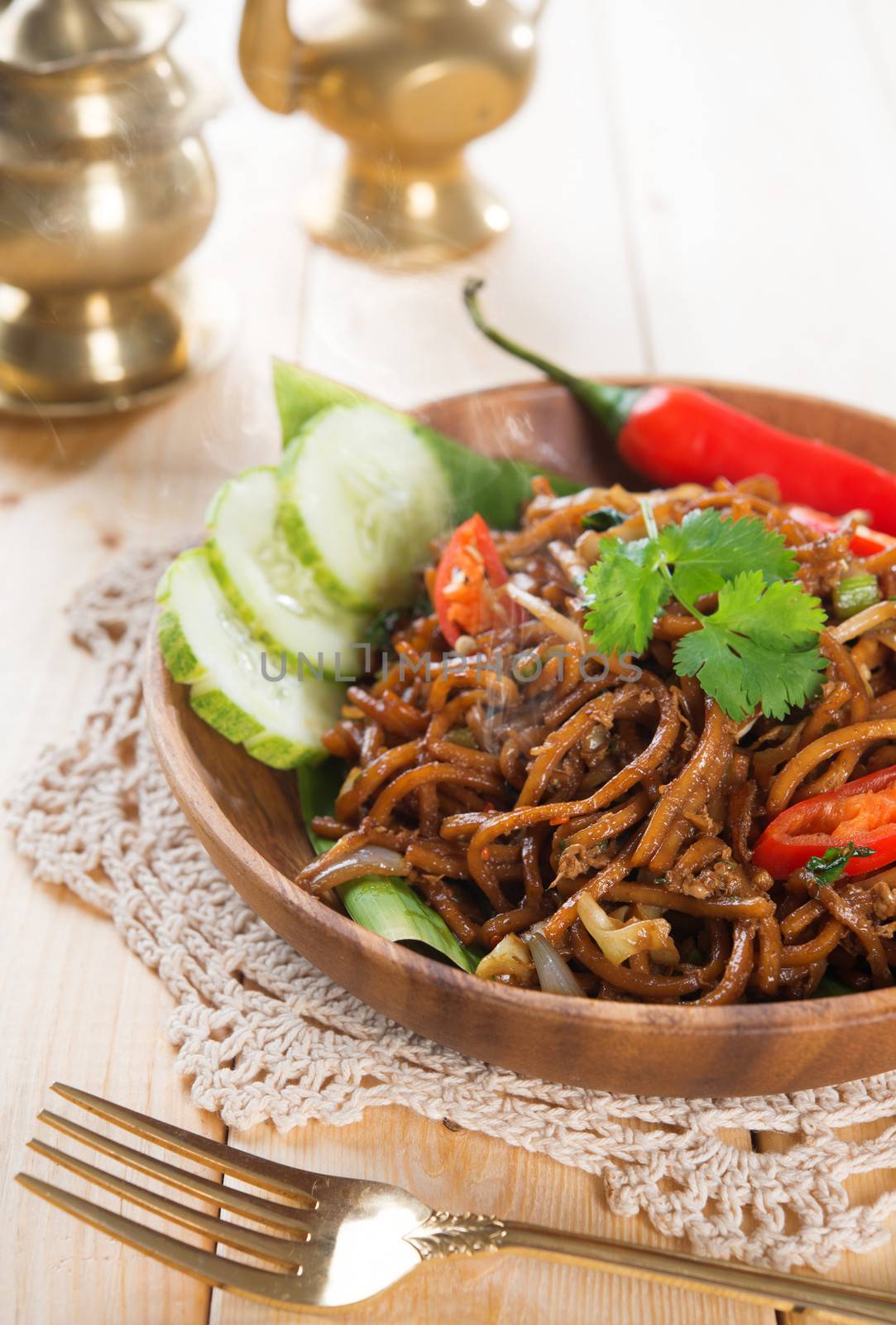 Spicy fried noodles. Indonesian and Malaysian cuisine, mi goreng or mee goreng mamak with wooden dining table setting. Fresh hot with steamed smoke.